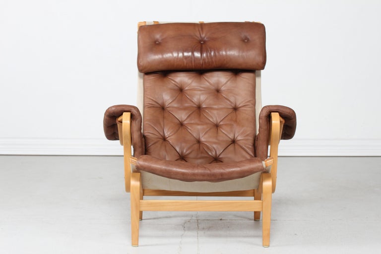 Pernilla easy chair by Swedish furniture designer Bruno Mathsson manufactured by Dux

The chair is made of lacquered steam bend beech stretched with canvas. Upholstery of light brown/cognac colored natural leather with good patina.

The