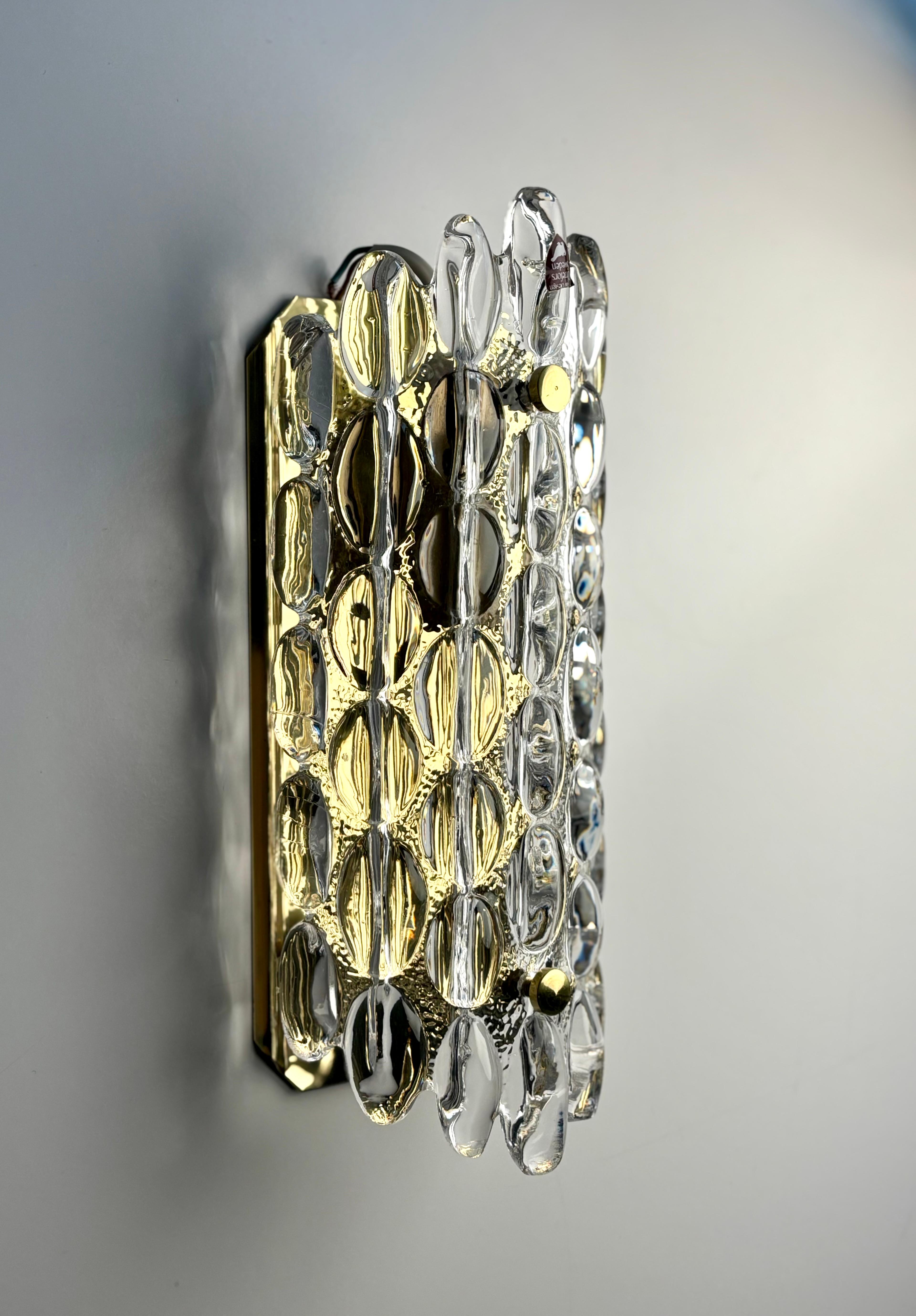 Elegante applique murale du designer suédois Carl Fagerlund pour Orrefors Glasbruk - modèle 2355 / 111. Le verre d'art en cristal lisse et épais, texturé par des bulles, forme une courbe sur la plaque en laiton brillant avec des détails en laiton -