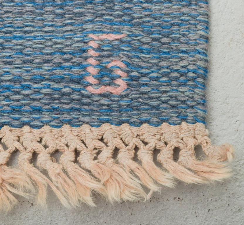 Schwedischer handgewebter Teppich aus reiner Wolle. Rölakan-Technik. 
Geometrisches Muster in den Farben Blau, Weiß und Rosa.
Entwurf: 