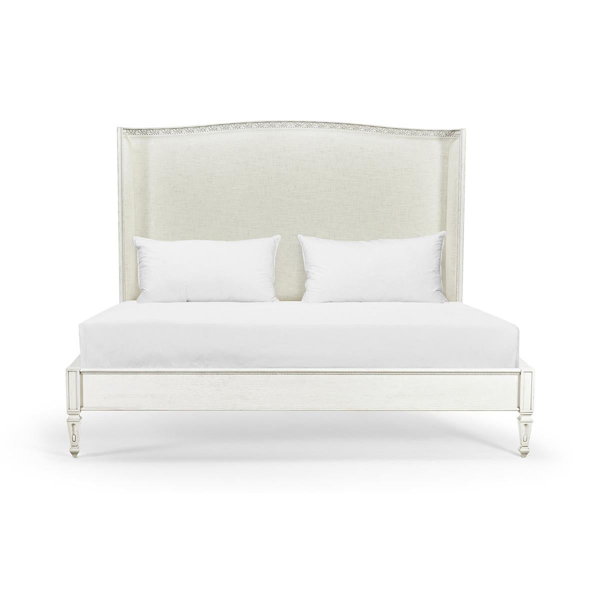 Swedish carved and painted king bed, with a wood frame that is embellished with floral motif trim wrapping around a shelter headboard upholstered in Belgian performance linen. Finished in chalk white, the elegant base is alighted upon a unique set