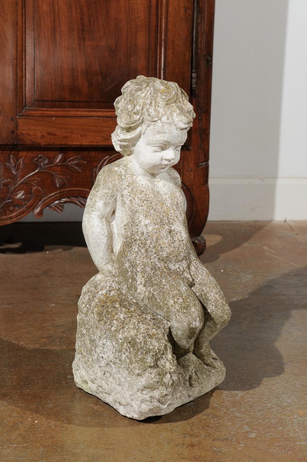 A Swedish carved stone garden sculpture from the 20th century, depicting a putto sitting on a rock. Created in Sweden during the 20th century, this carved stone sculpture charms us with its wonderful wear and patina, surrounding a charming scene. A
