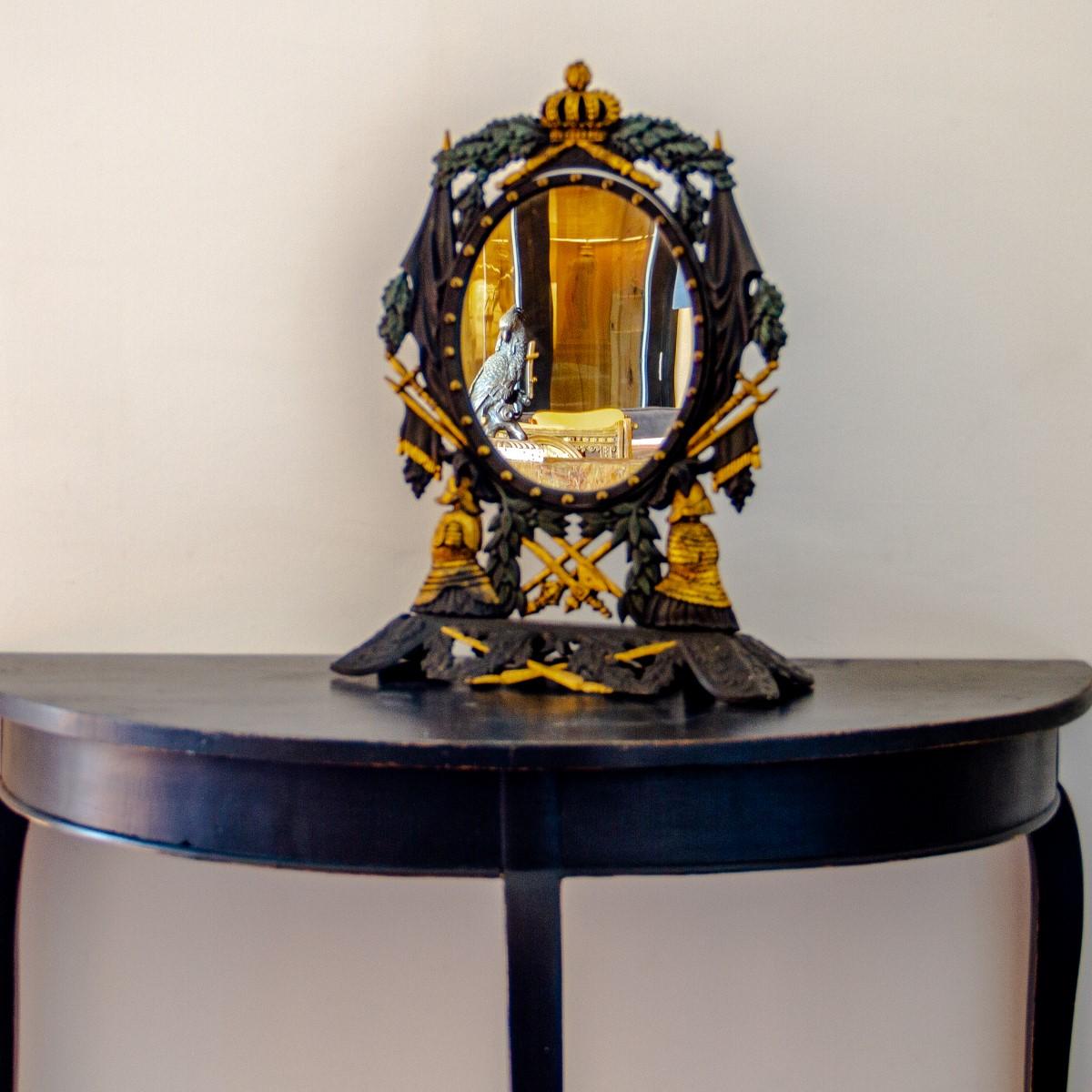 A Swedish cast iron table mirror in the neoclassical manner, with oak leaf detail and gilt painted royal symbols of a crown, weapons and flanked with helmeted figures. The central oval mirror pivots and is decorated with gilt beading, circa 1840.