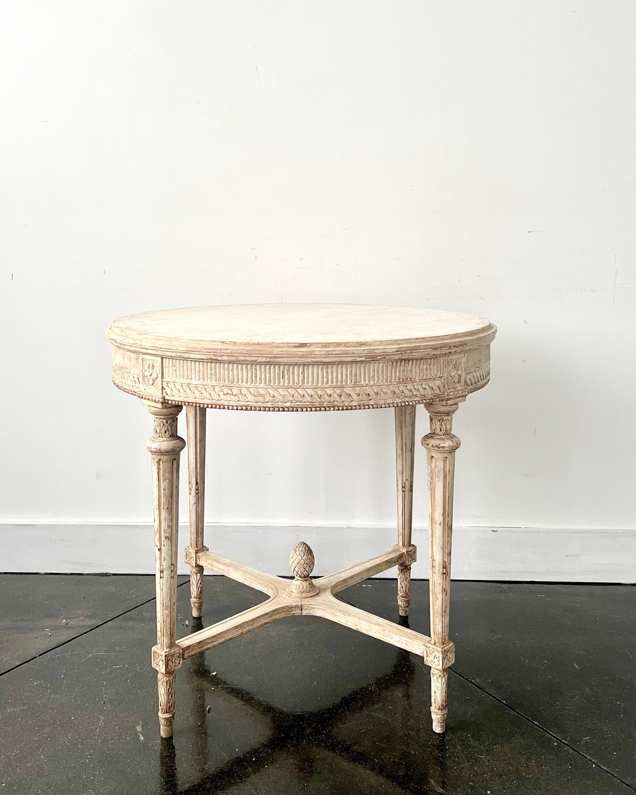 Swedish Gustavian style round center table with very richly carved apron, tapering carved legs and saltire strecher with central medallion in painted worn cream patina, Sweden, circa 1860.