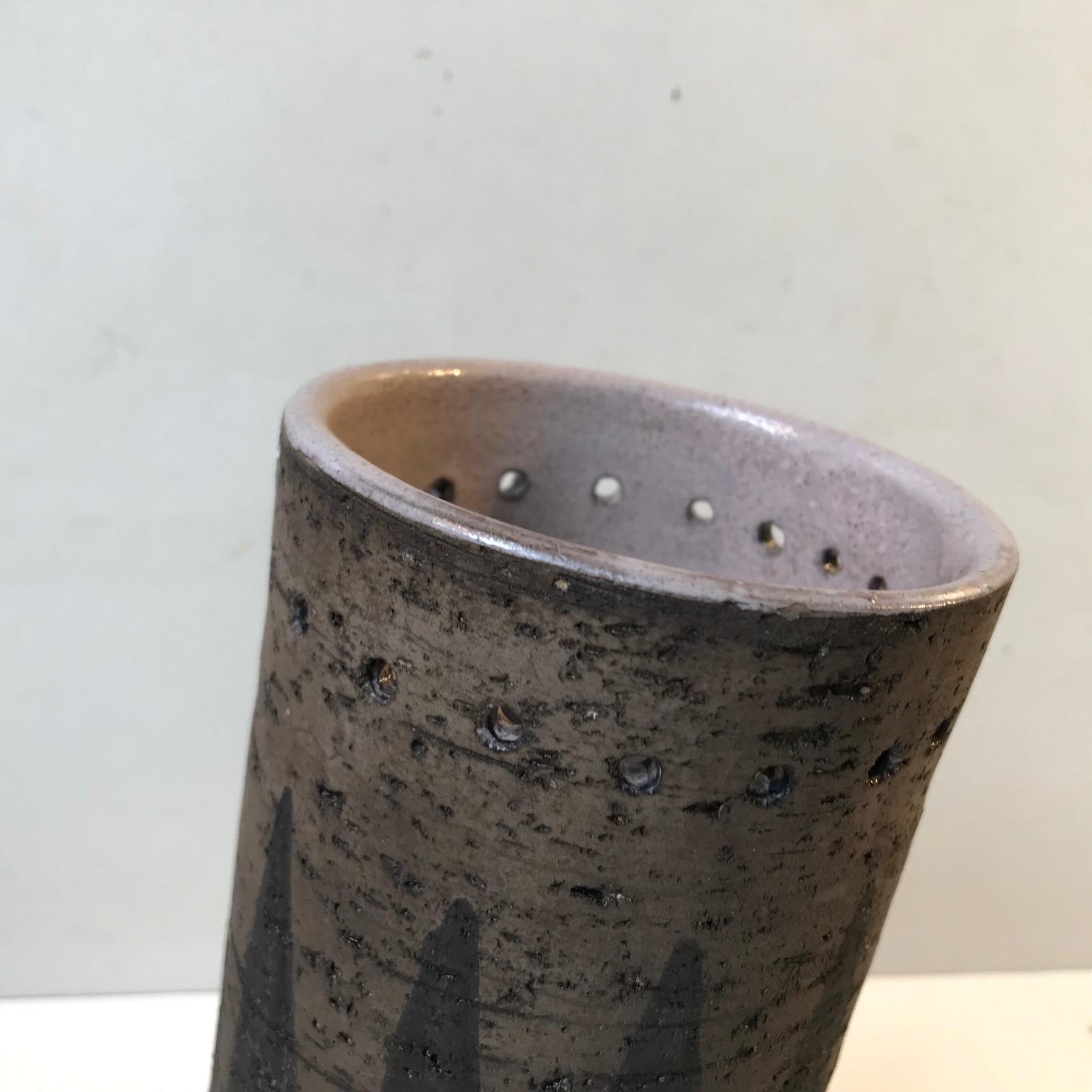 Unusual and unique cylindrical vase in chamotte clay. Partially unglazed exterior decorated with black arrow and see-through horizontal piercings. The interior is fully glazed for practical reasons. It was designed during the early 1970s by ceramist