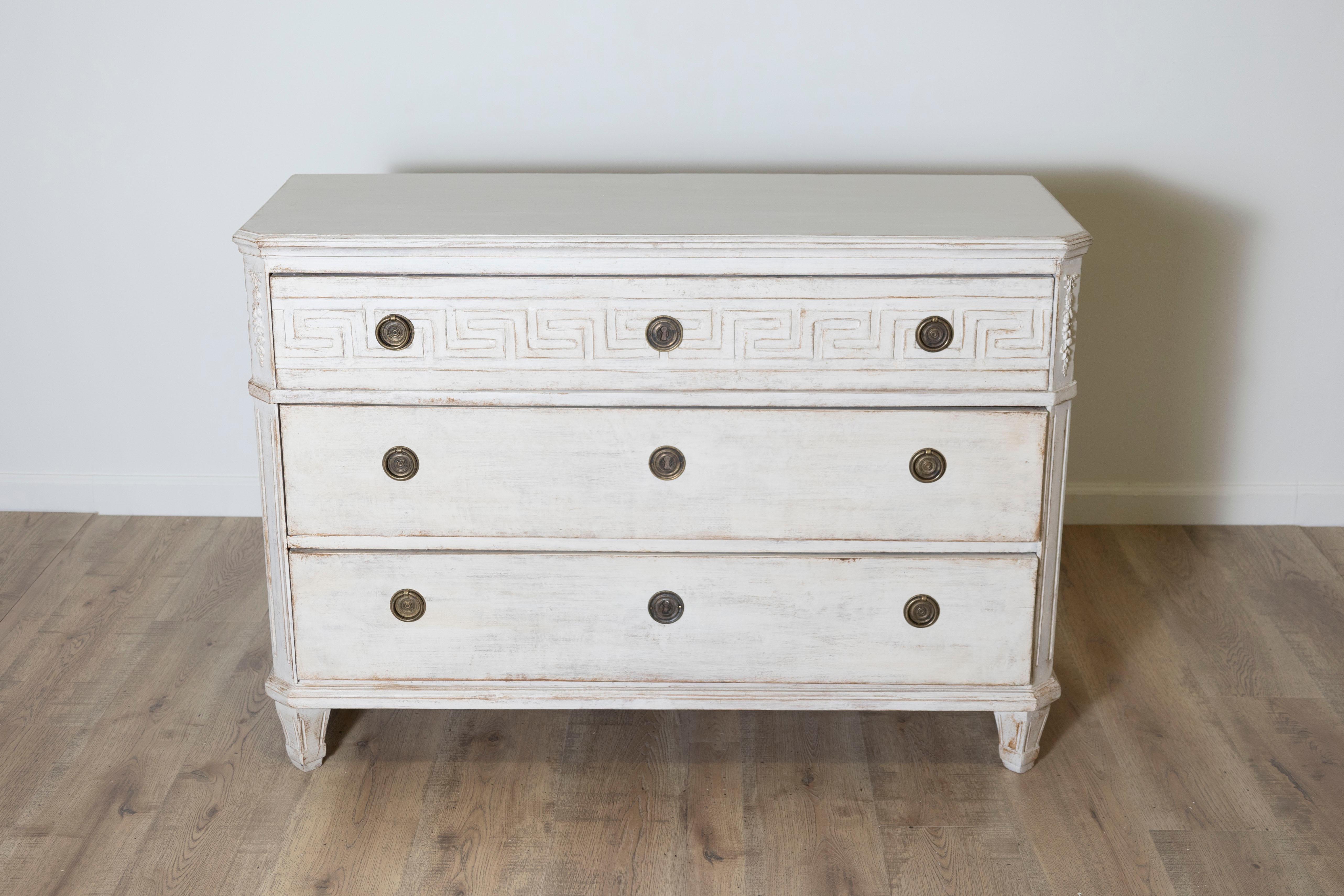 This stunning Swedish chest of drawers beautifully blends neoclassical design elements with the clean lines characteristic of Gustavian style. Constructed from pine wood and finished with a softly distressed white paint, it showcases an aged patina