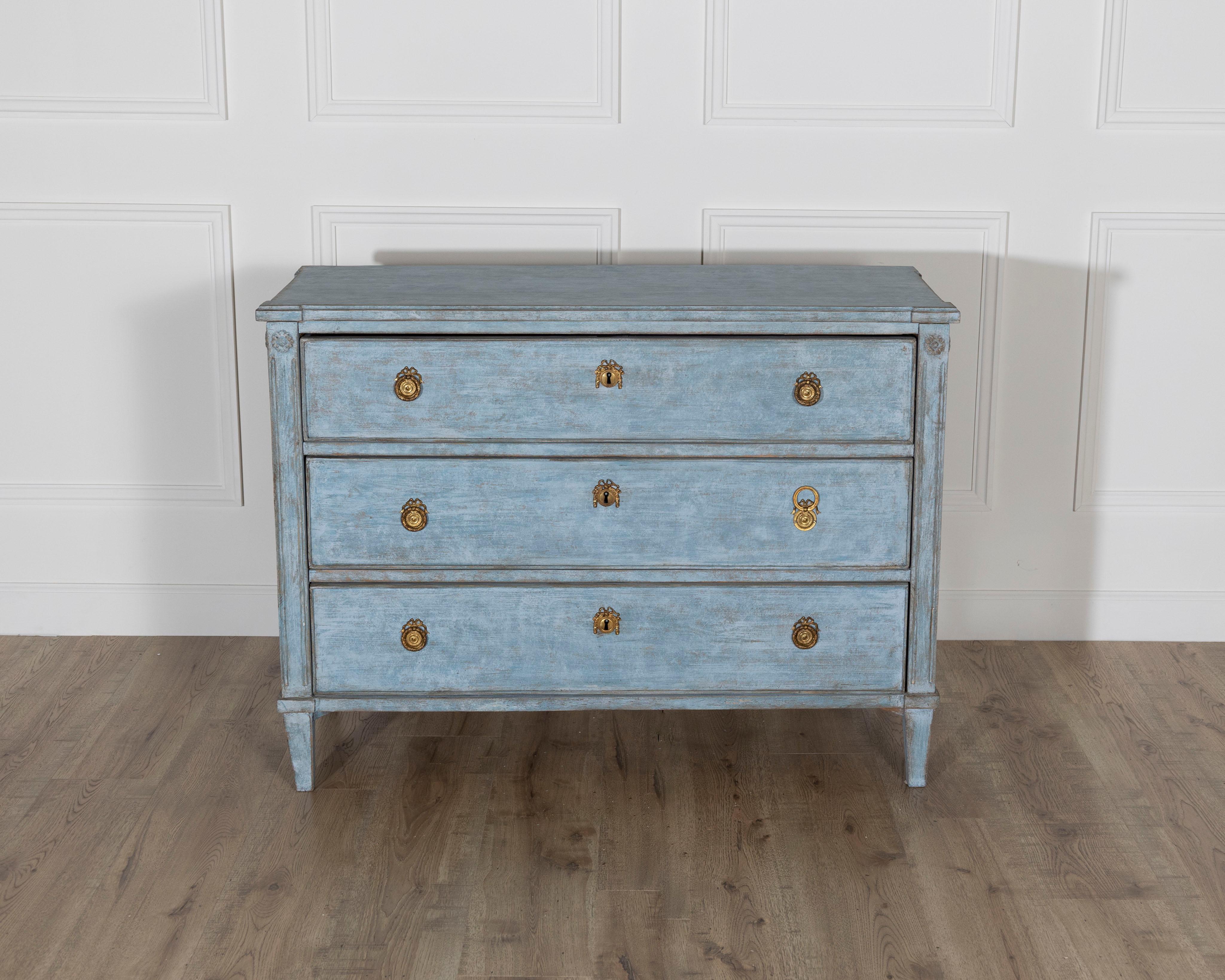 A beautifully proportioned Swedish chest of drawers from around 1860, featuring its original carved details and a soft blue painted finish with a delicately aged patina. The clean neoclassical silhouette, with three full-length drawers, gently