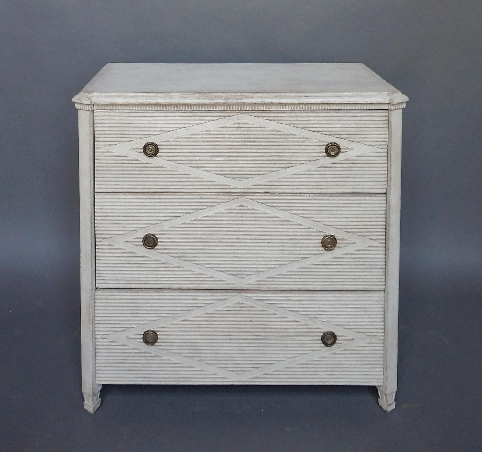 Three-drawer chest, Sweden, circa 1890, in the Gustavian Style. Dentil detail under the shaped top, canted corners, and square feet. The drawer fronts have the original brass pulls and recessed lozenges in the over-all horizontal reeding.  No