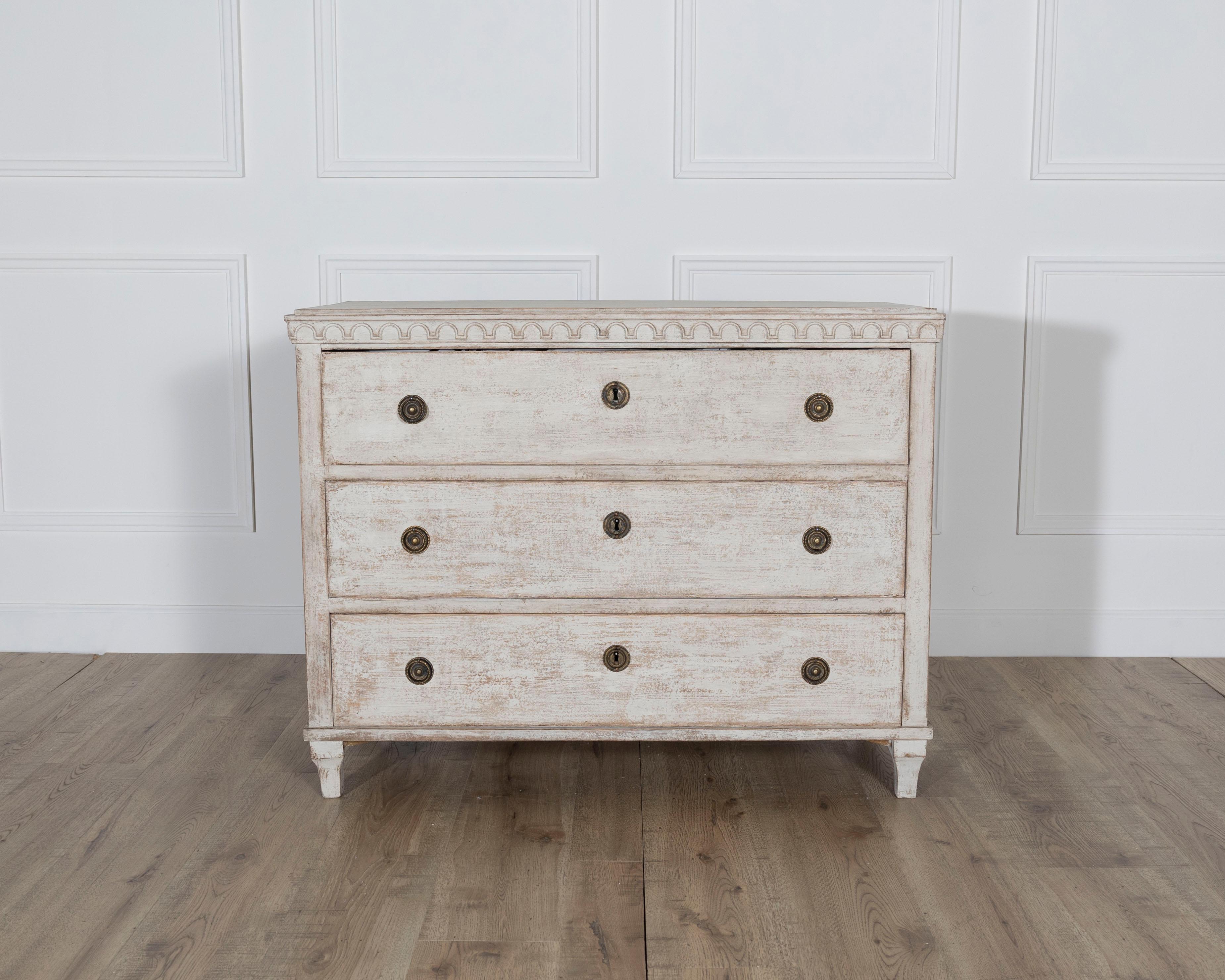 A stately Swedish chest of drawers from the mid-1800s, blending neoclassical form with country charm. Crafted from pine and finished in a soft, chalky white paint with natural wear, this three-drawer commode features clean lines, subtle molding, and