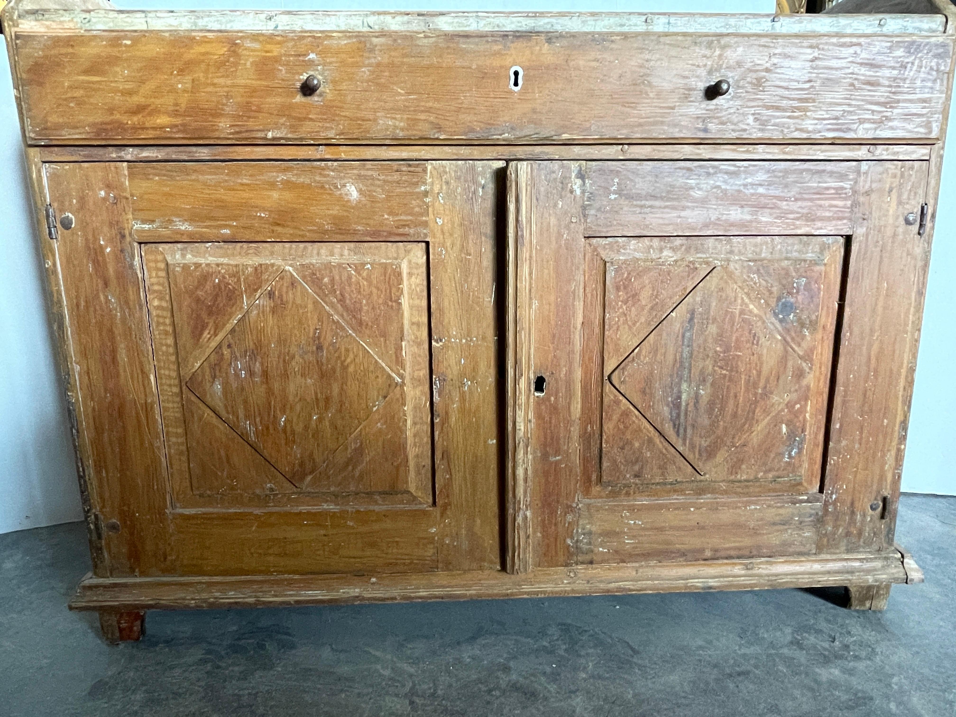 This 19th century Gustavian style buffet originated from Sweden. It has wonderful craftmanship throughout with hand carved wooden pulls, wood pegging, faux marbleized paint on the top and even hand carved feet.
The front face diamond shape on the