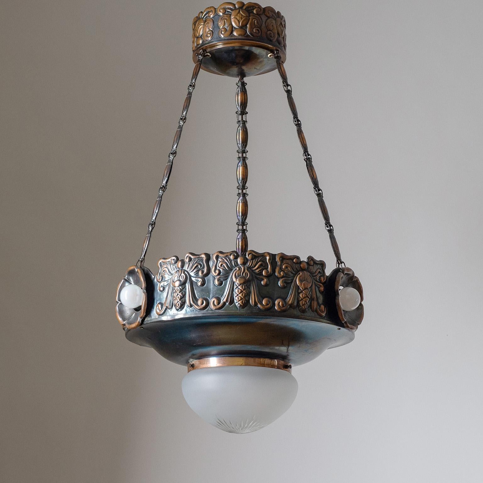 Fine Swedish Jugendstil suspension light from the 1910-1920s. The body is made entirely of copper, heavily embossed with floral and angel-like motifs. There are three lights embedded around the rim and a central one with a cut satin glass diffuser.