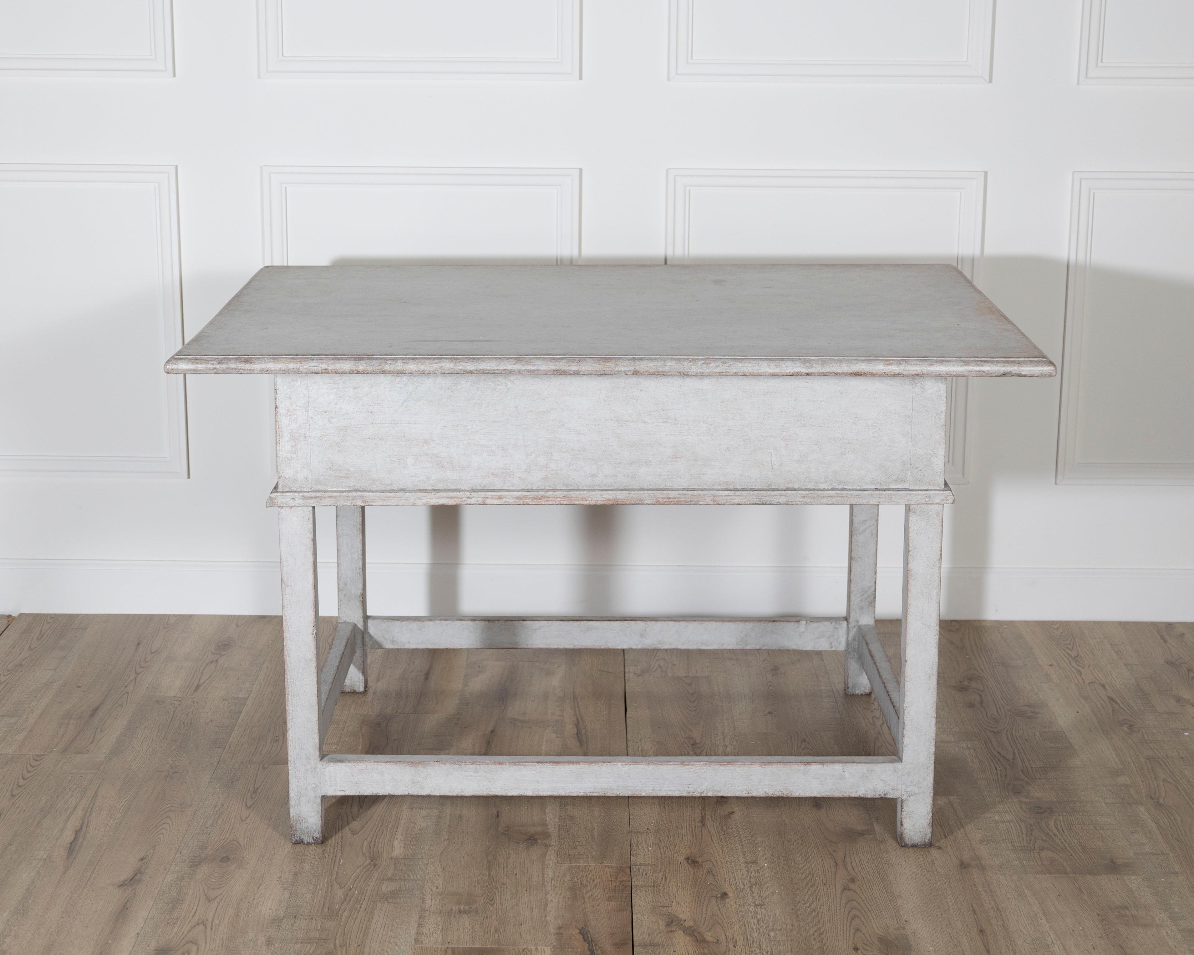A rustic yet refined Swedish country table from the second half of the 19th century, crafted in solid pine. The rectangular top rests above a simple apron fitted with a deep, centrally located drawer, accented by a brass pull in its center. The