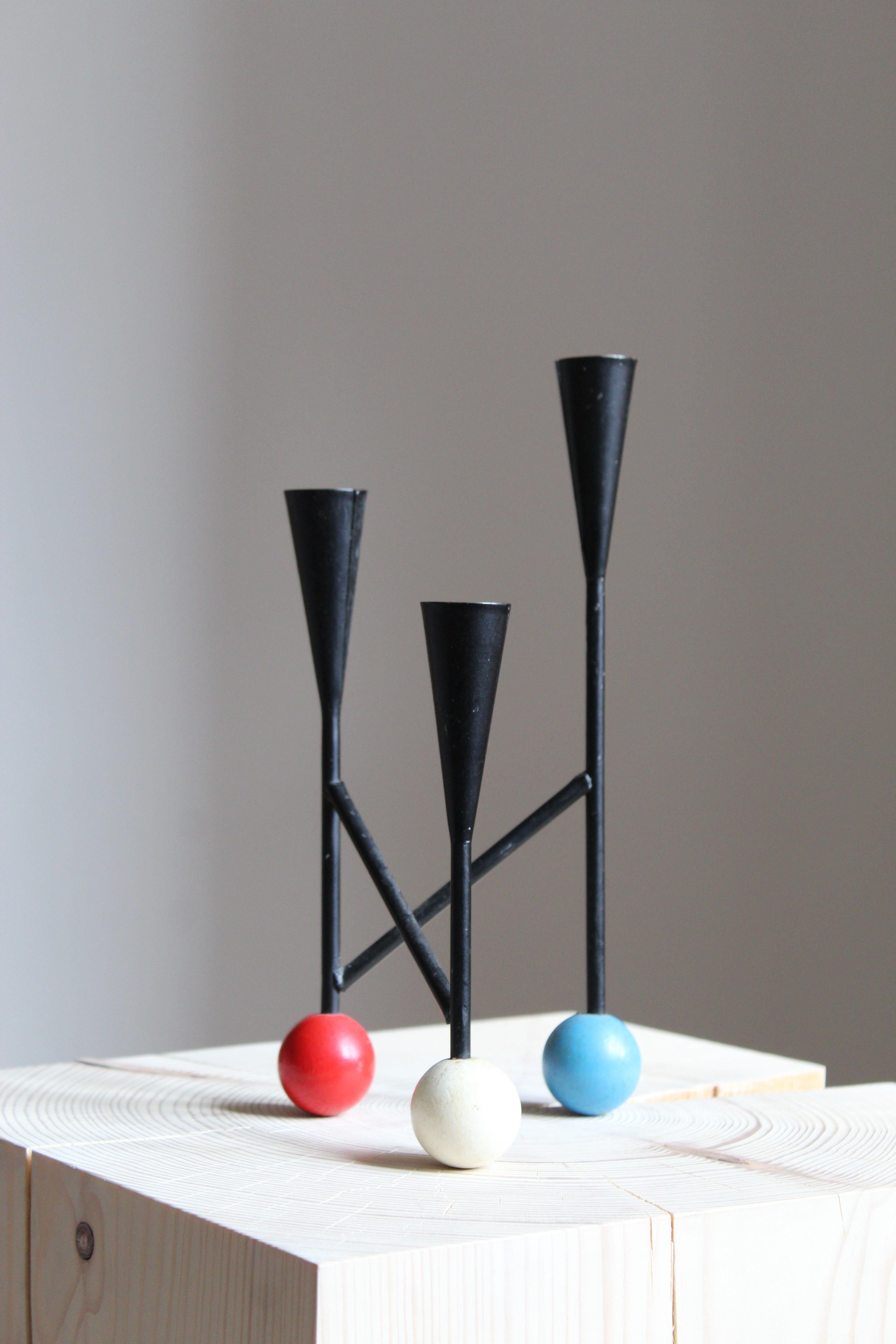 A small modernist candelabra or candle tree, circa 1970s. In black painted metal, wooden feet in white, blue and red. Fits 3 normal-sized Scandinavian candles.