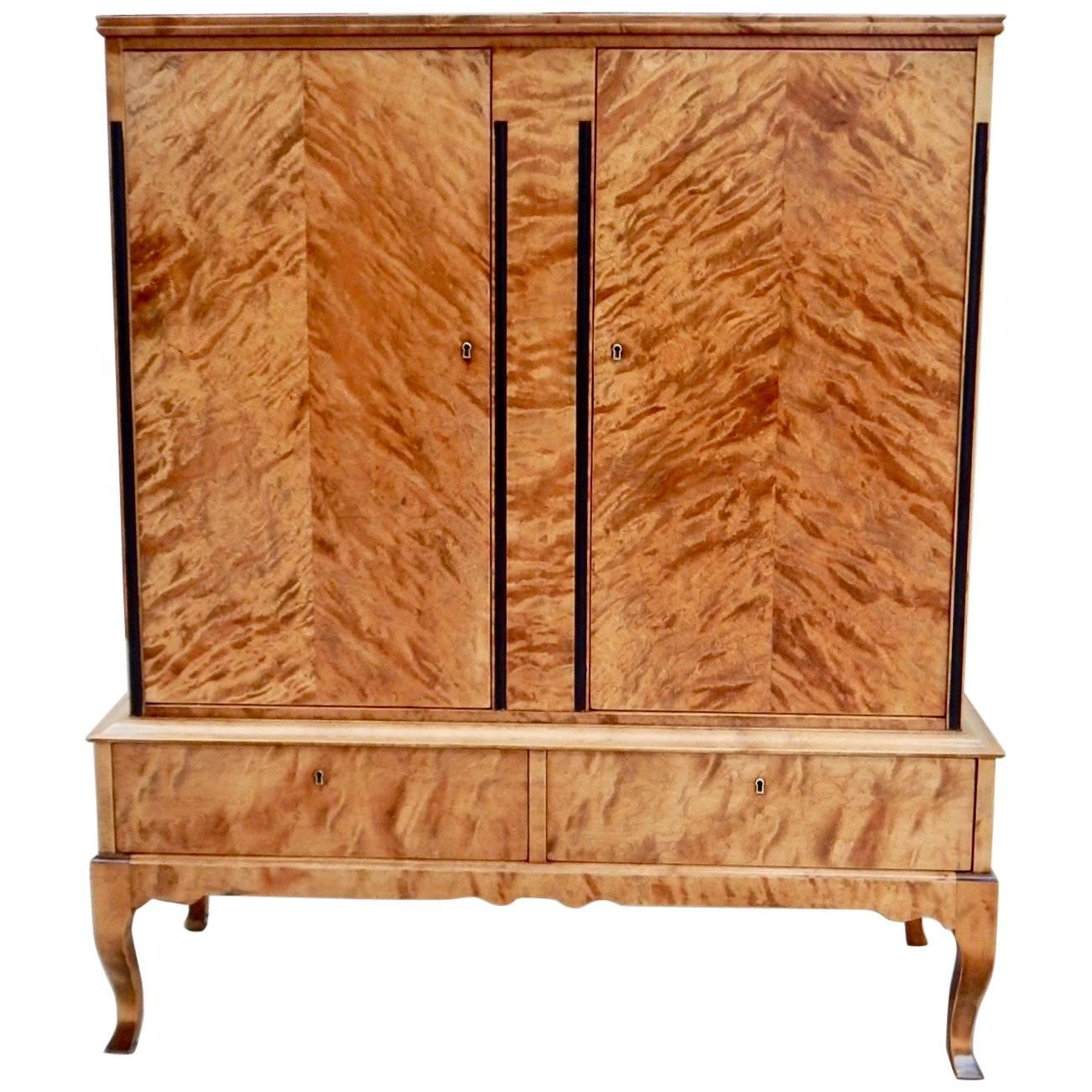 Swedish Art Deco era Biedermeier revival storage cabinet. Rendered in highly figured golden flame birch wood. With two adjustable and removable shelves. With two exterior drawers with dovetailed joinery. With original key. This item has just been