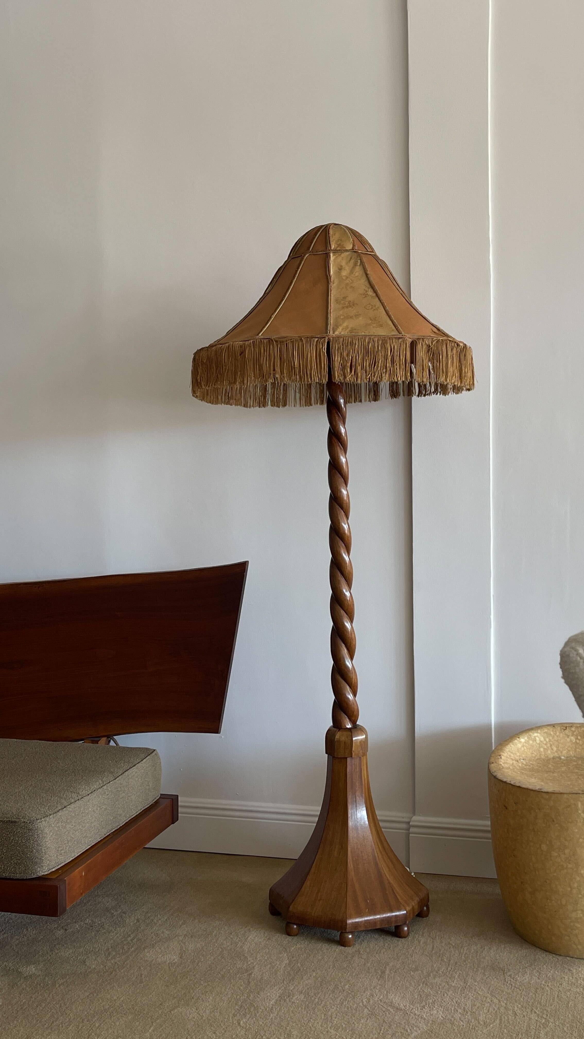 A carved wooden floor lamp produced in Sweden, c. 1930s  with original fabric lampshade with fringes.