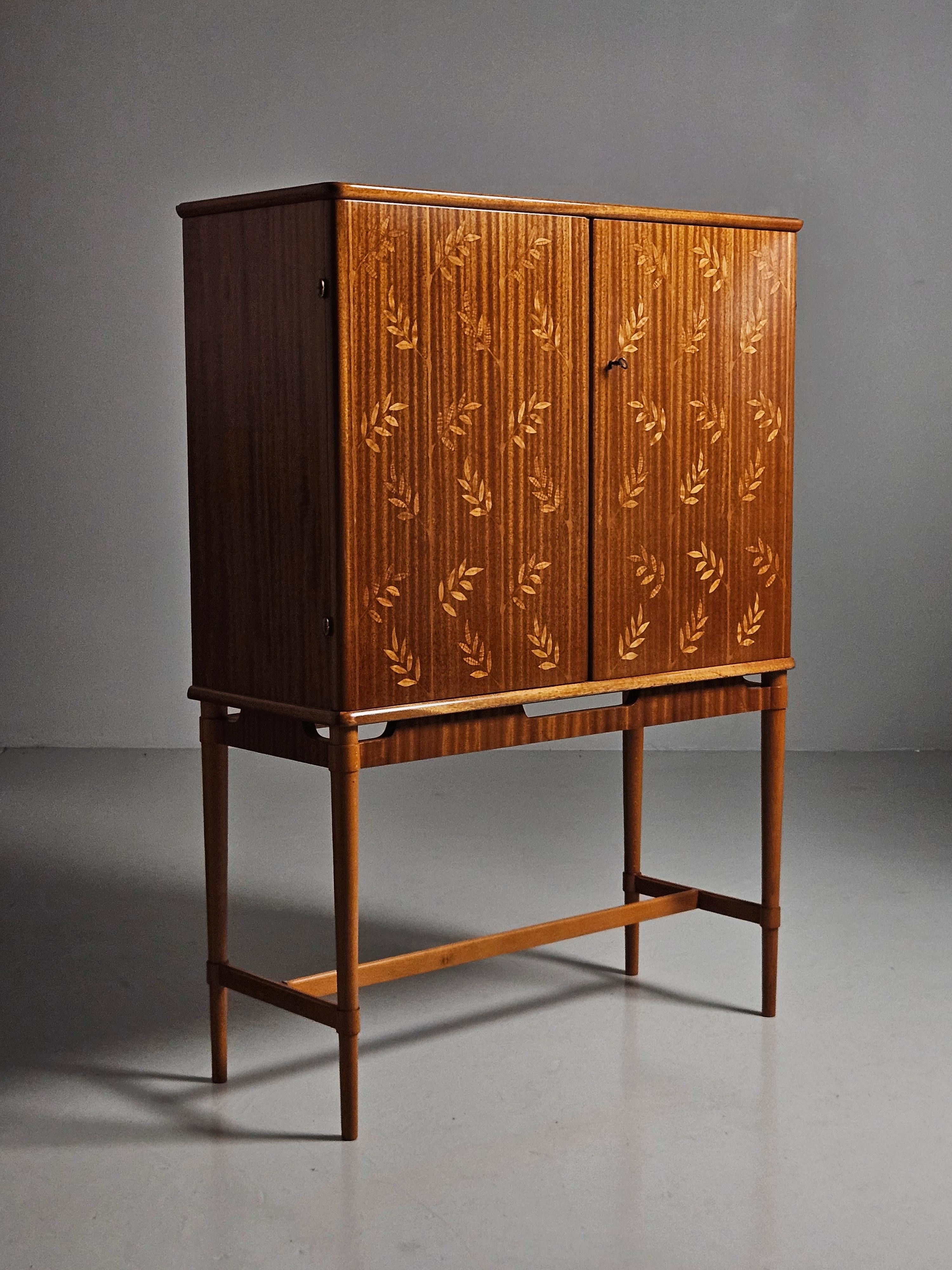 Beautiful bar cabinet attributed to designer Erik Mattsson and produced by Möbelbolaget Tranås, Sweden, during the 1940s. 

Scandinavian modern at its best. Made in mahogany with beautiful leaf inlays. Lighting on the inside with shelves and mirror