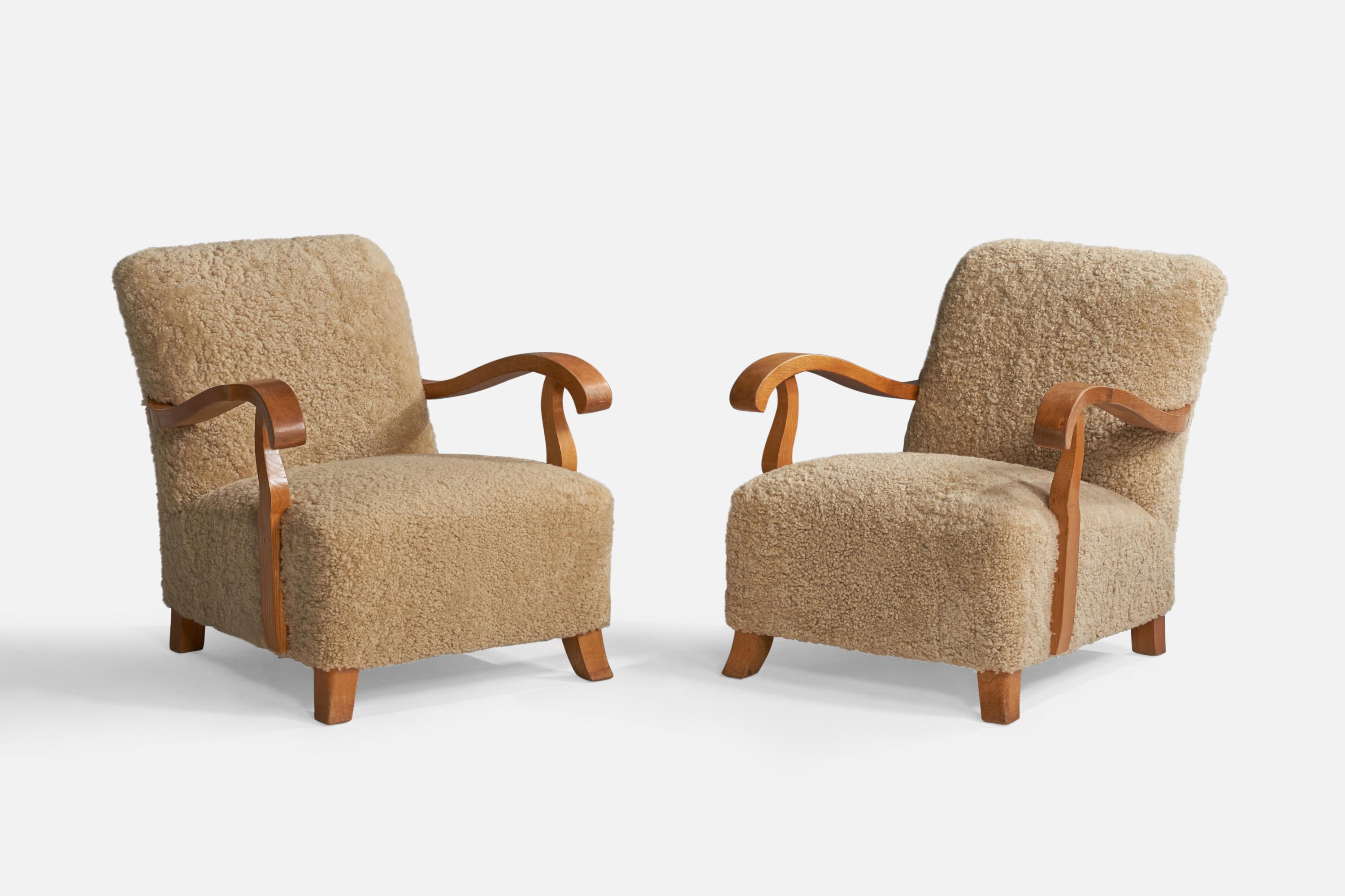 A pair of beige shearling and oak lounge chairs designed and produced in Sweden, c. 1940s.