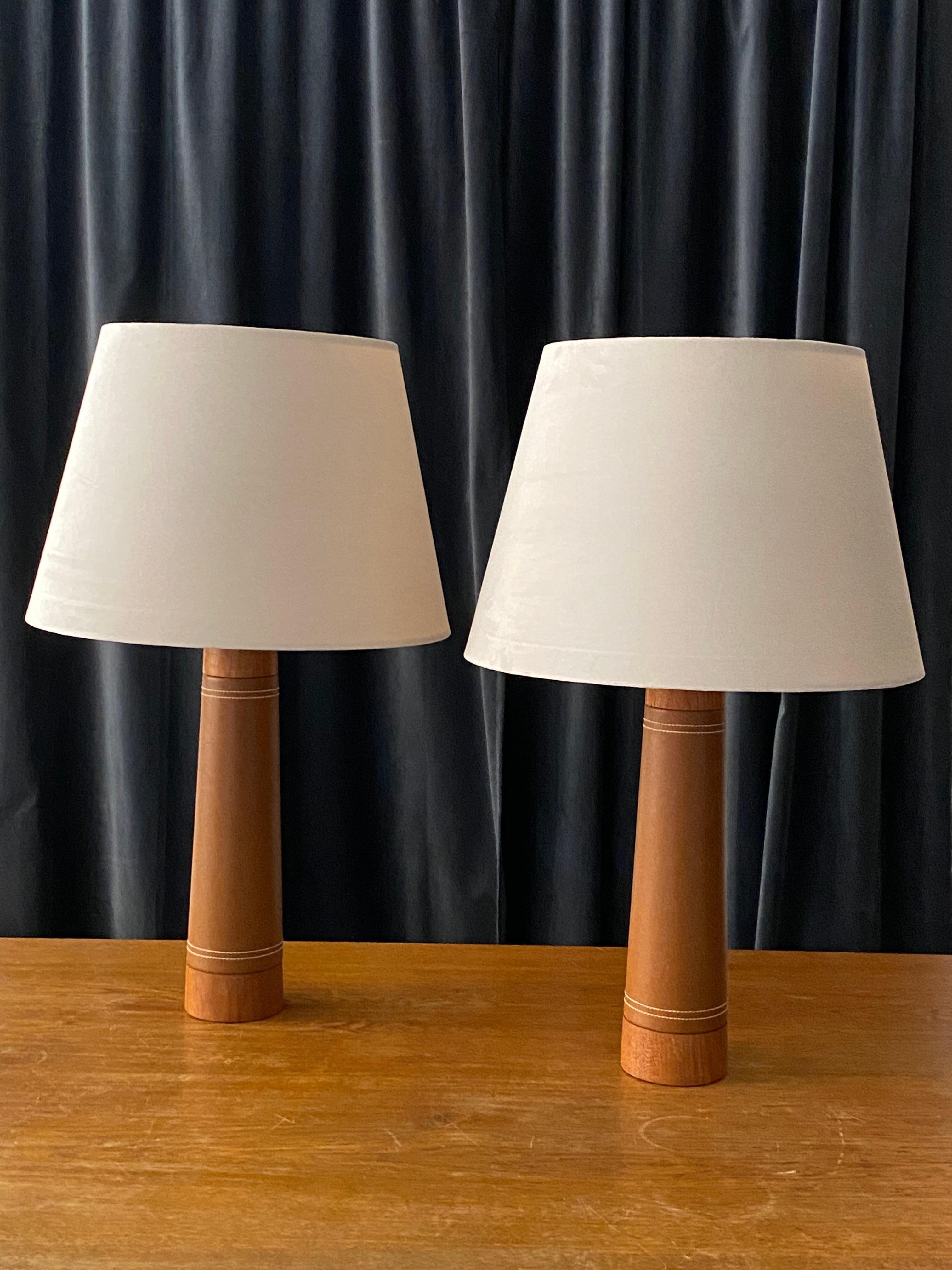 A pair of Minimalist table lamps, designed and produced in Sweden, circa 1960s. In solid sculpted teak and leatherette with contrasting stitching. 

Lampshades are attached for reference. Sold without lampshades. Measurements stated are of bases.
