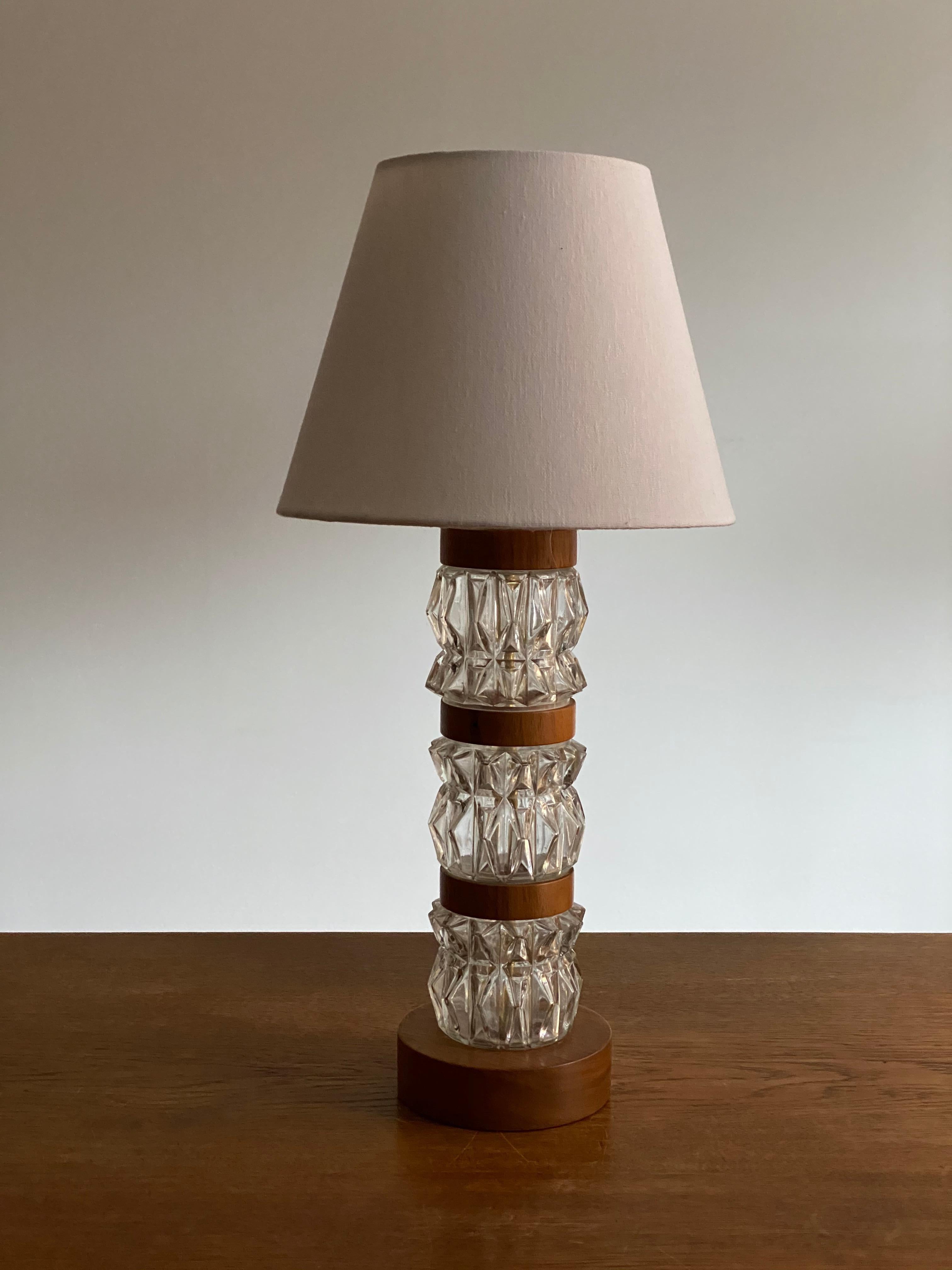 A highly modernist organic table lamp. Of Swedish production. In highly ornamented art glass, incorporates wooden ribbons in teak veneer.

The lampshade is not included in the purchase. Stated measurements are without a lampshade. Lampshade can be