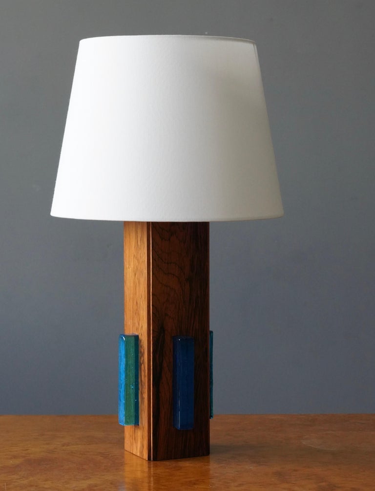 A sculptural and minimalist table lamp. In rosewood and blue glass. Designed and produced in Sweden, 1950s-1960s.

Dimensions listed are without shade. 
Dimensions with shade: height is 21.25 inches, width is 12 inches.
Dimensions of shade: top