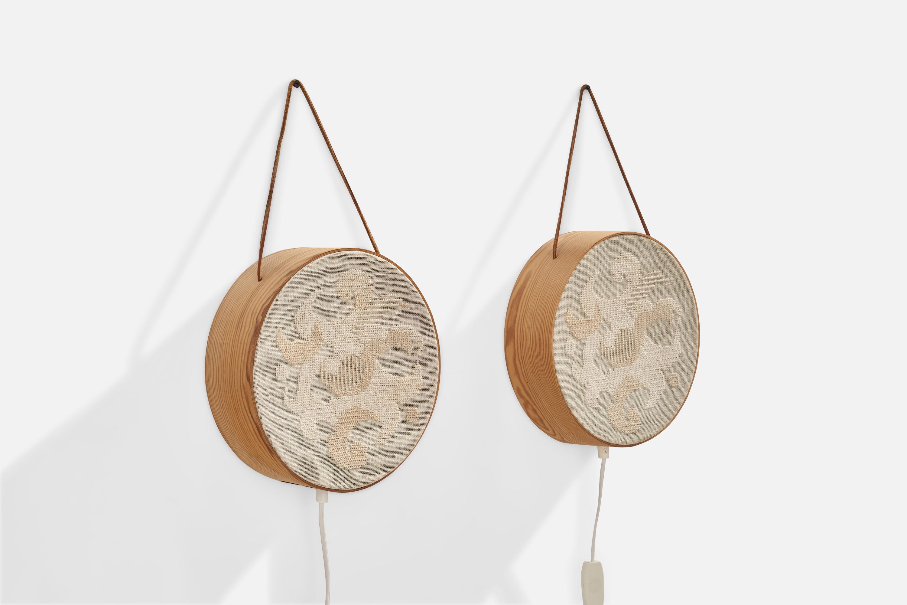 A pair of pine, leather and beige embroidery fabric wall lights designed and produced in Sweden, 1970s.

Overall Dimensions (inches): 3.25”  H x 10” D
Back Plate Dimensions (inches): N/A
Bulb Specifications: E-14 Bulb
Number of Sockets: 2
All