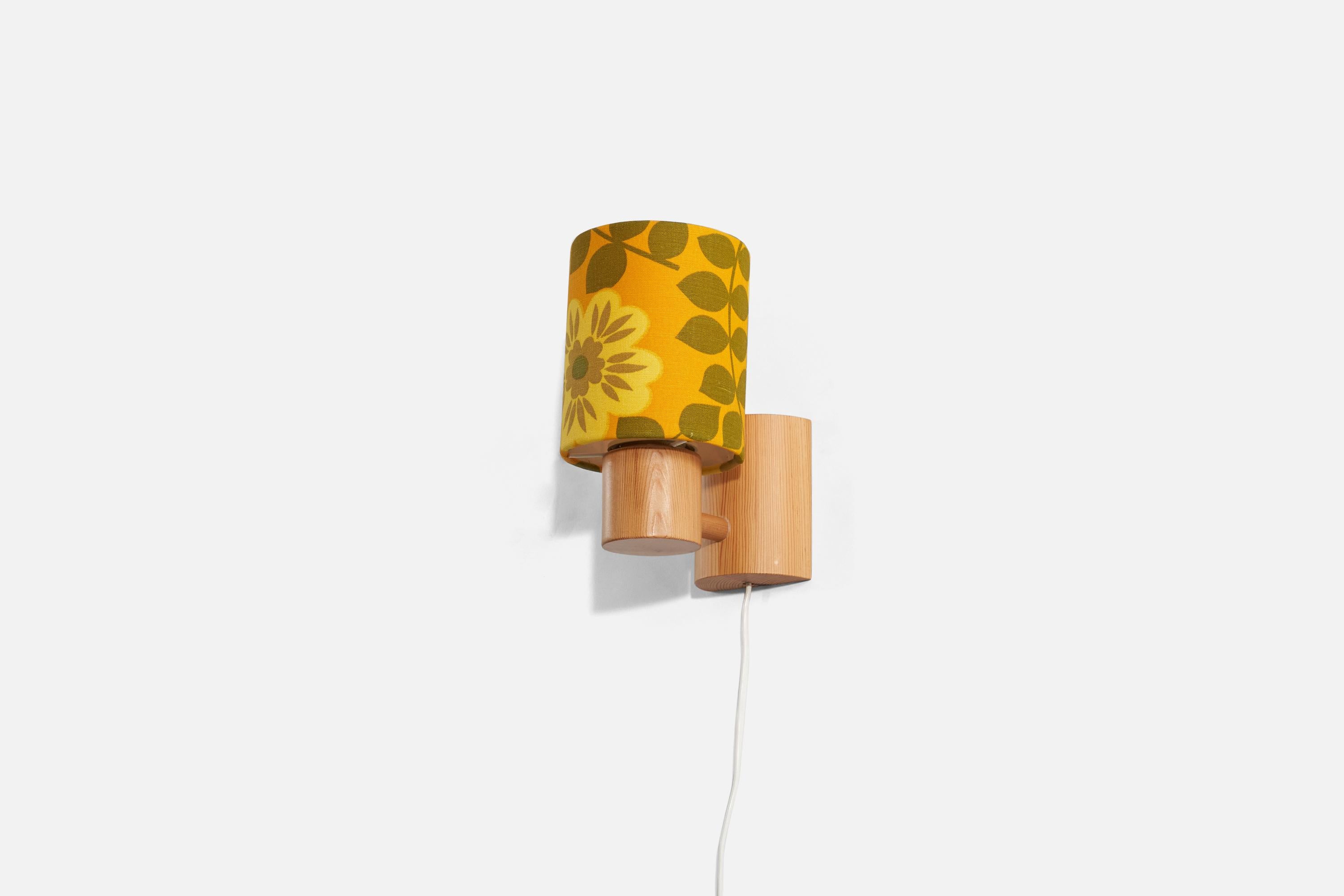 A solid pine wall light featuring a fabric lampshade with a green and yellow floral motif; designed and produced in Sweden, 1970s. 

Dimensions of the back plate (inches) : 4 x 3.25 x 1.6875 (H x W x D).