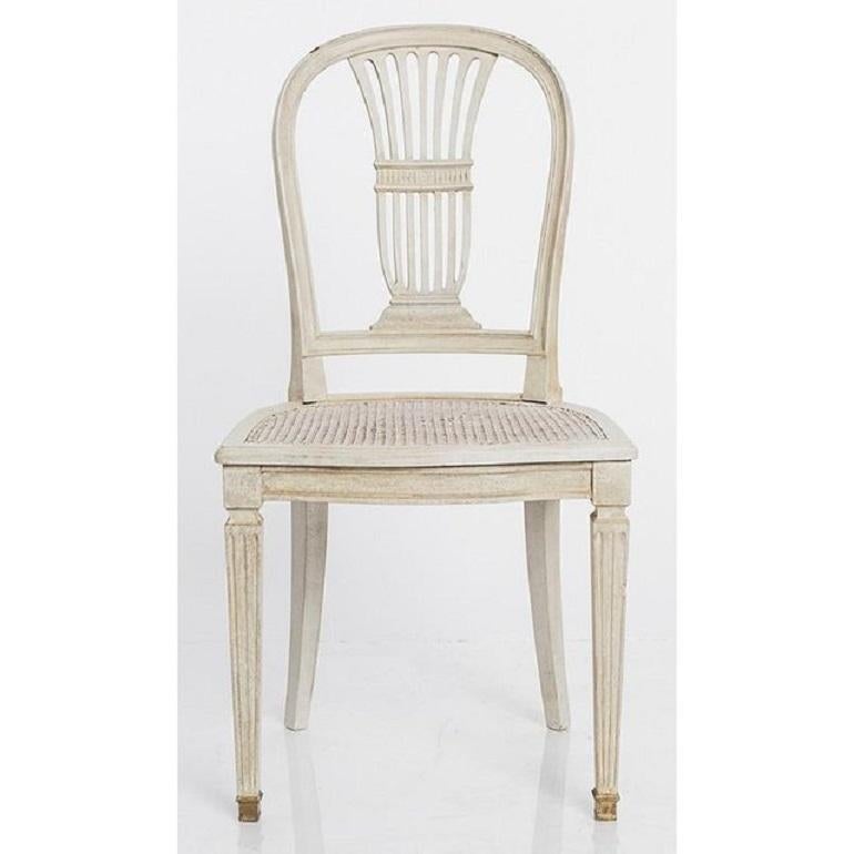 Wonderful set of provincial dining chairs, made in Sweden at the turn of the century. Decorated with classic details in the Gustavian style, like a wheat sheaf backrest and supported by fluted legs. Woven cane seat was later white-washed to match