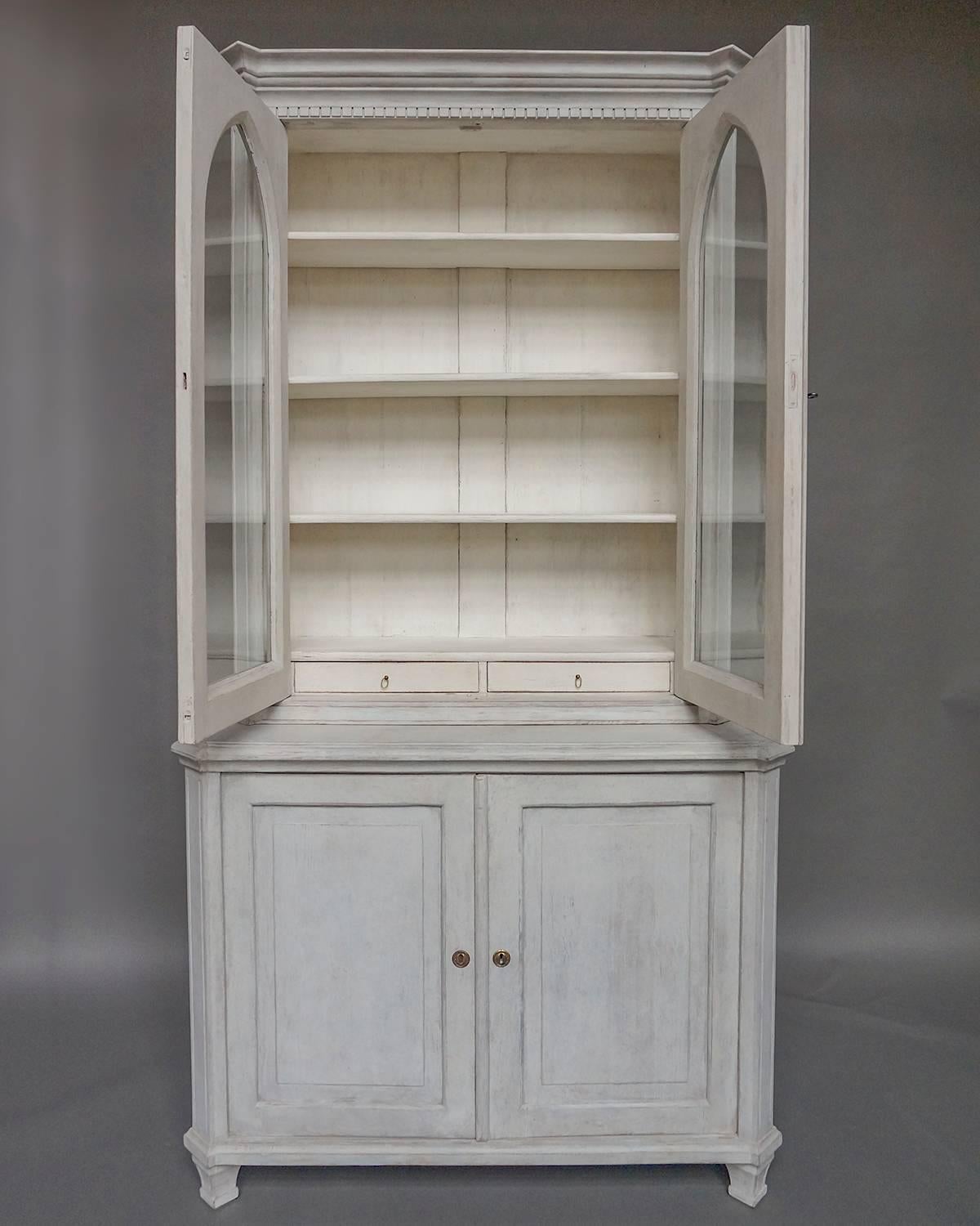 Cabinet in two parts, Sweden, circa 1870. The upper section has double doors with Gothic arched windows which retain their original glass. At the top is a bold cornice with dentil detail. The lower section has two panelled doors concealing a large