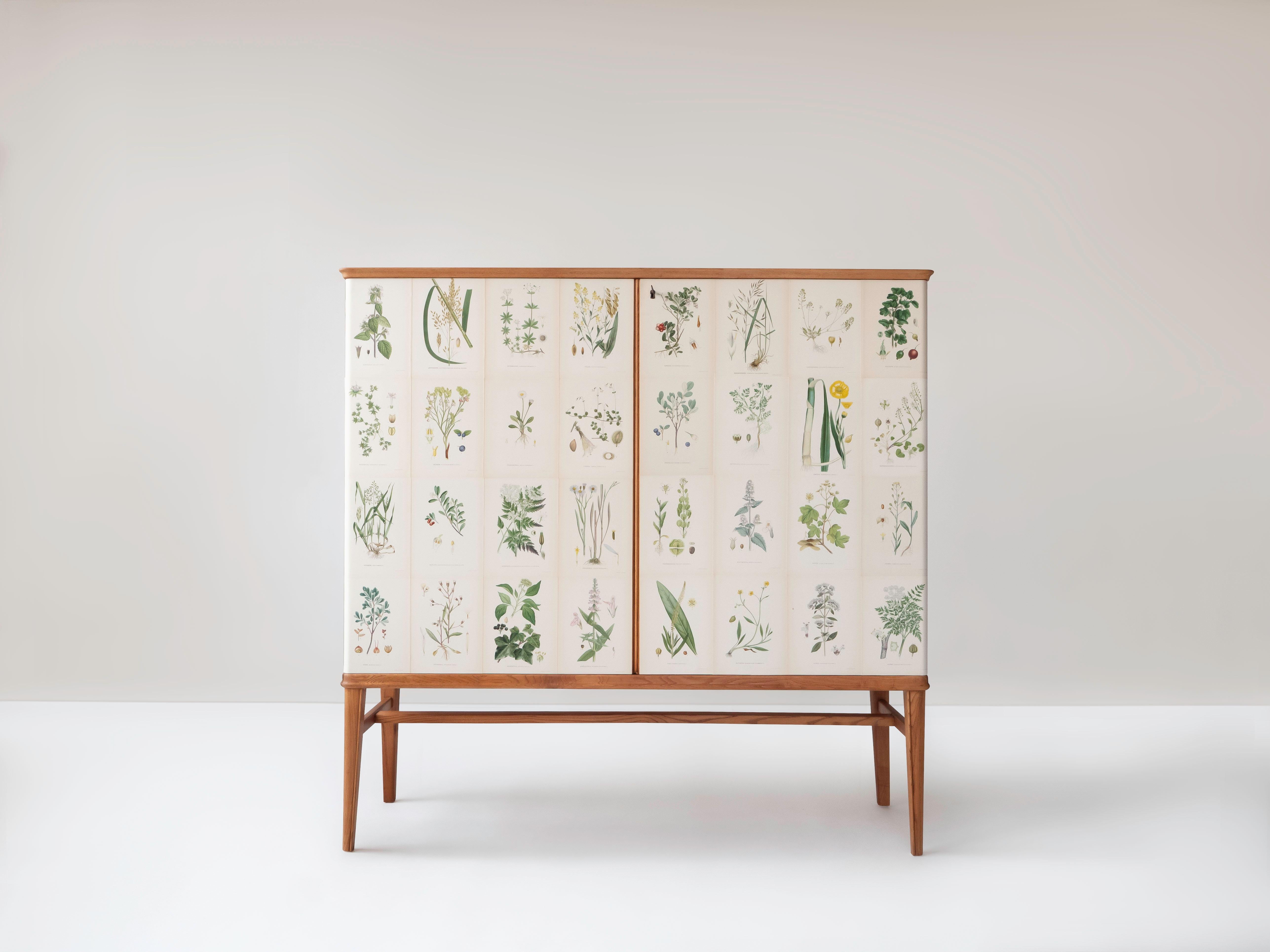 A Swedish sideboard or cabinet in Elm, circa 1940's. The rectangular cabinet is covered with early Norden's Flora Illustrations by C.A. Lindman. The cabinet has two locking doors that conceal 2 removable shelves and 5 pull adjustable drawers. It is