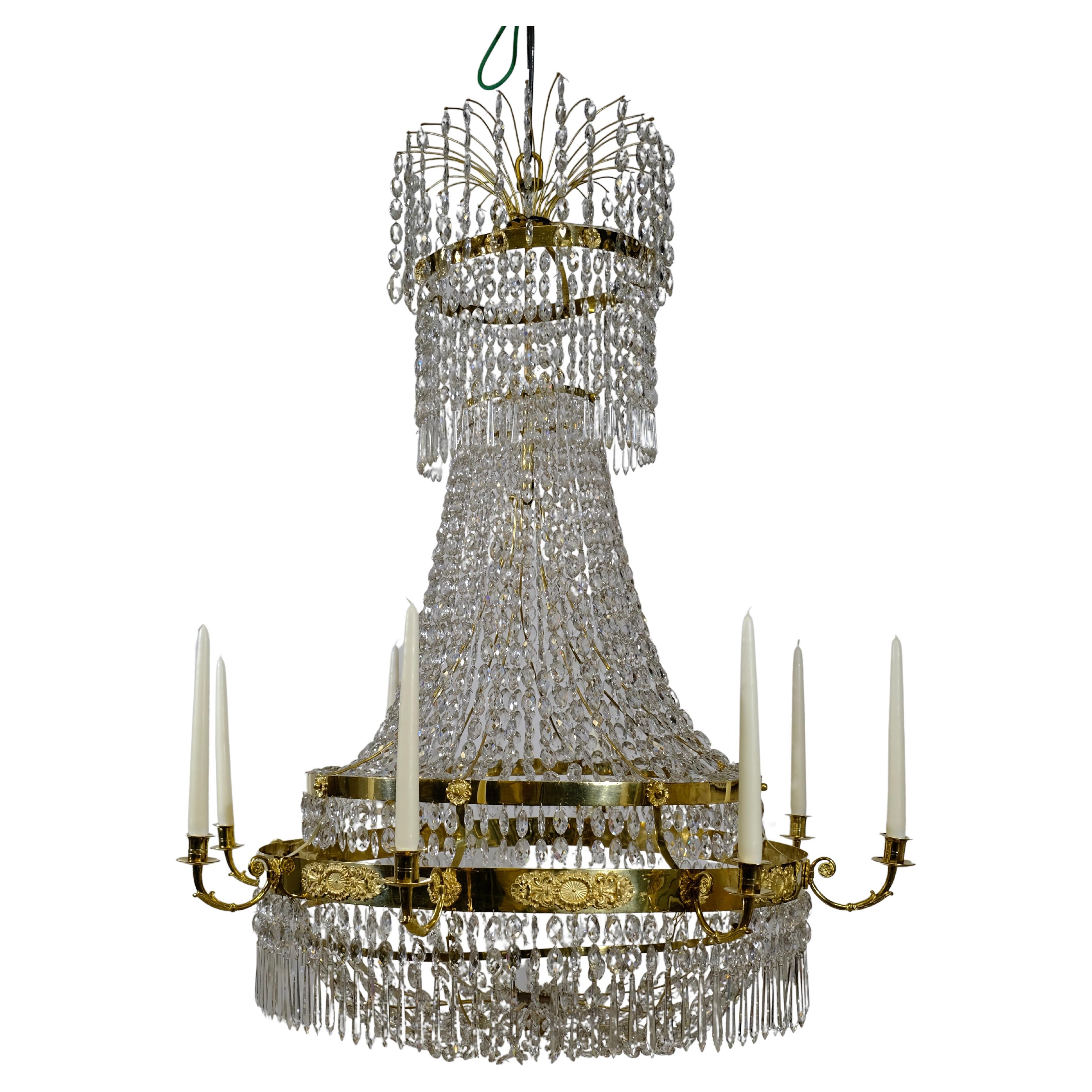A large and very fine Swedish Empire gilt-brass and cut-glass chandelier from the early 19th century. The corona hung with chains of drops and overall hung with beaded chains, the central tier issuing twelve scrolled candle arms above scroll