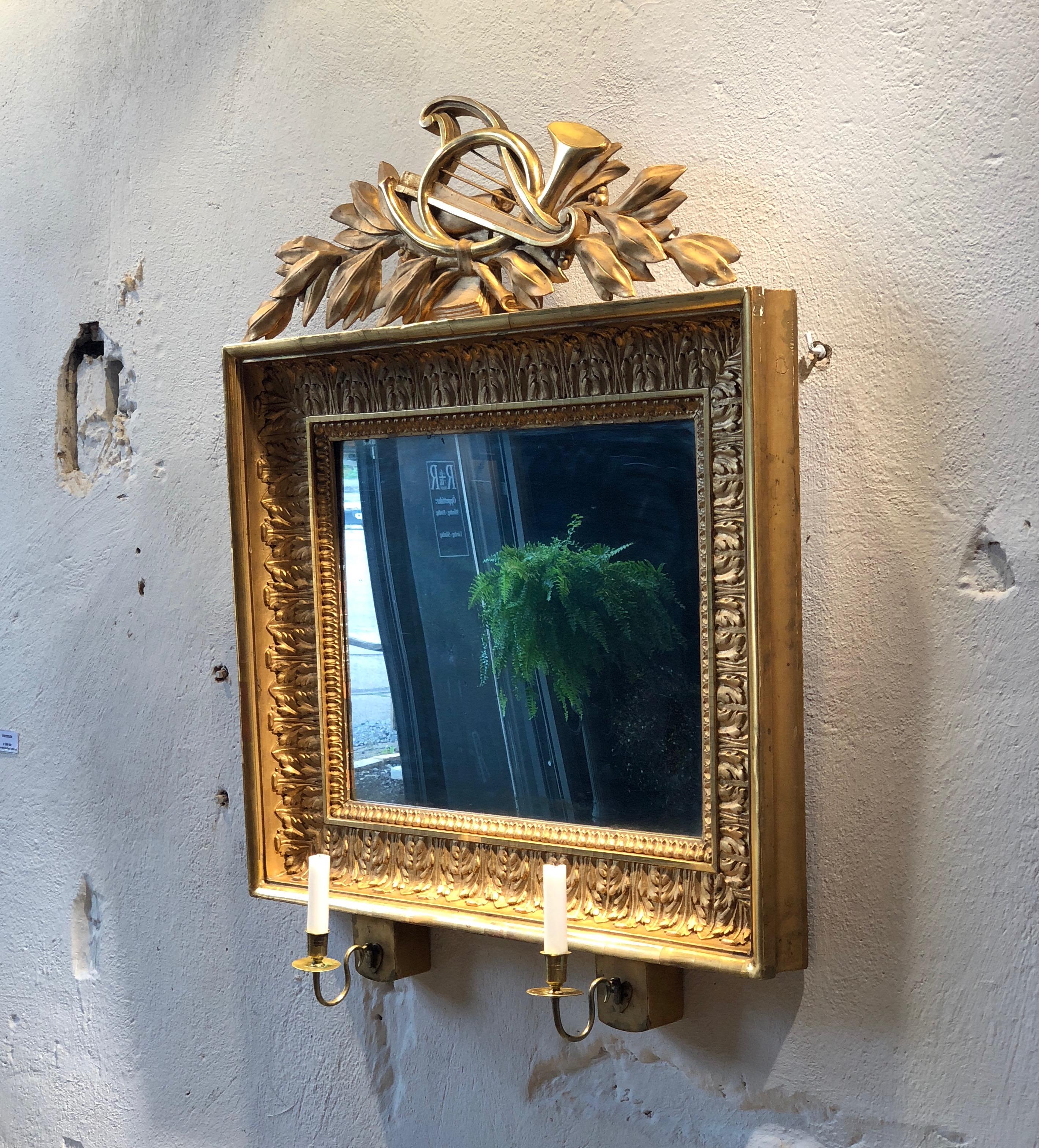 A Swedish Empire, mirrored wall sconce in a gilded frame with carved decorations showing trumpet and harp. Holders for two candles in brass.
Original gild and original mirror glass.