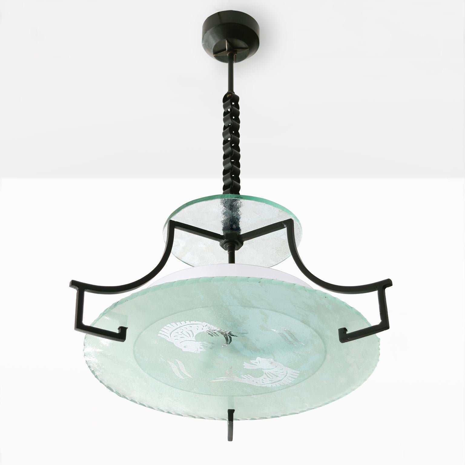 A Swedish Grace, Art Deco period etched glass and wrought iron chandelier. The fixture has a large acid etched flat glass shade with two fish and stylized wave designs. A tripod iron frame holds a second glass shade suspended above a frosted white