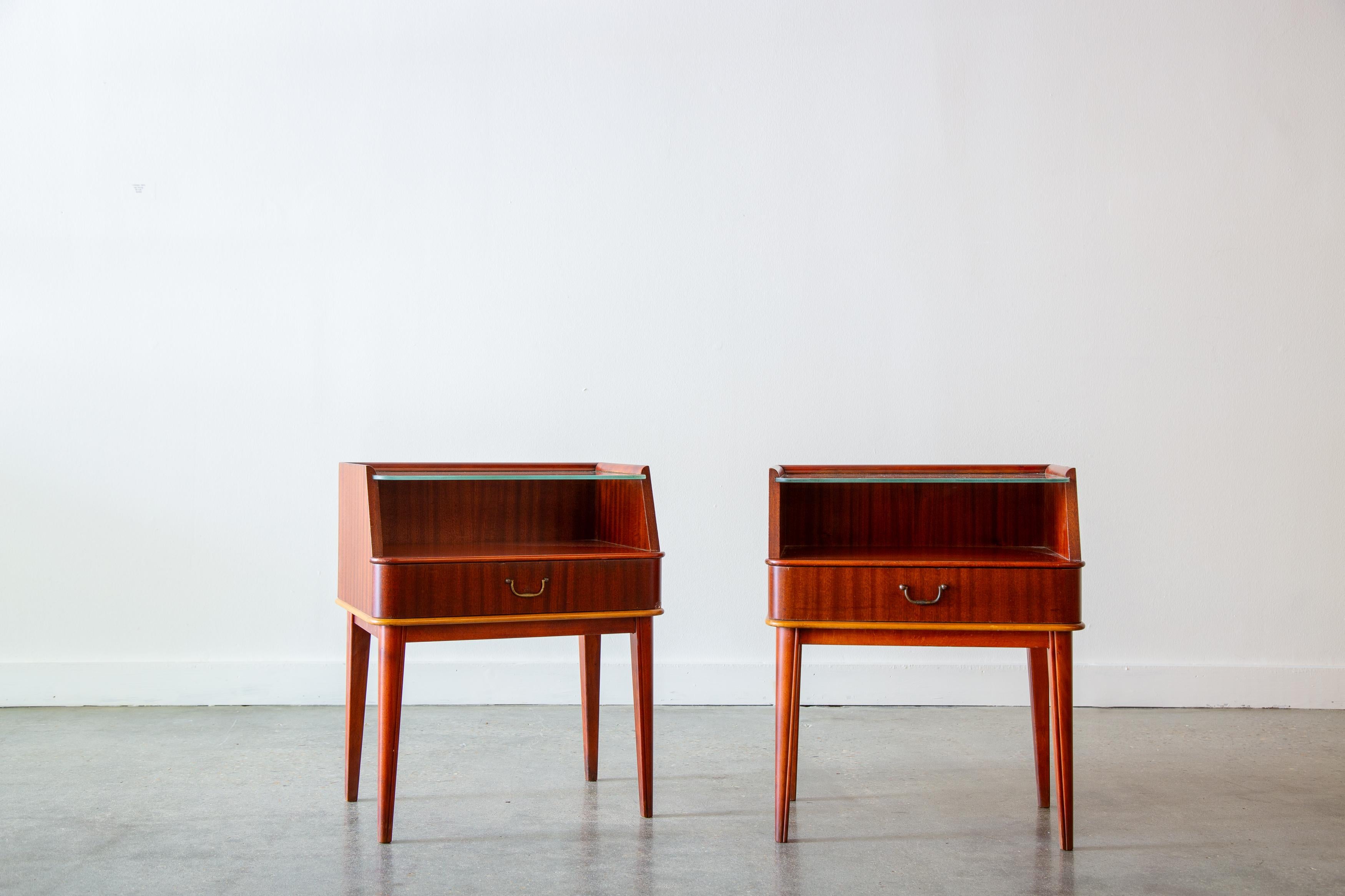 A pair of 1950s Swedish Art Deco end tables in Flame mahogany with birch fillet by Bodafors. The tops are in etched glass with a diamond pattern.  Which reflects through to the lower shelf with a lamp or upper lighting.  Storage drawers with brass