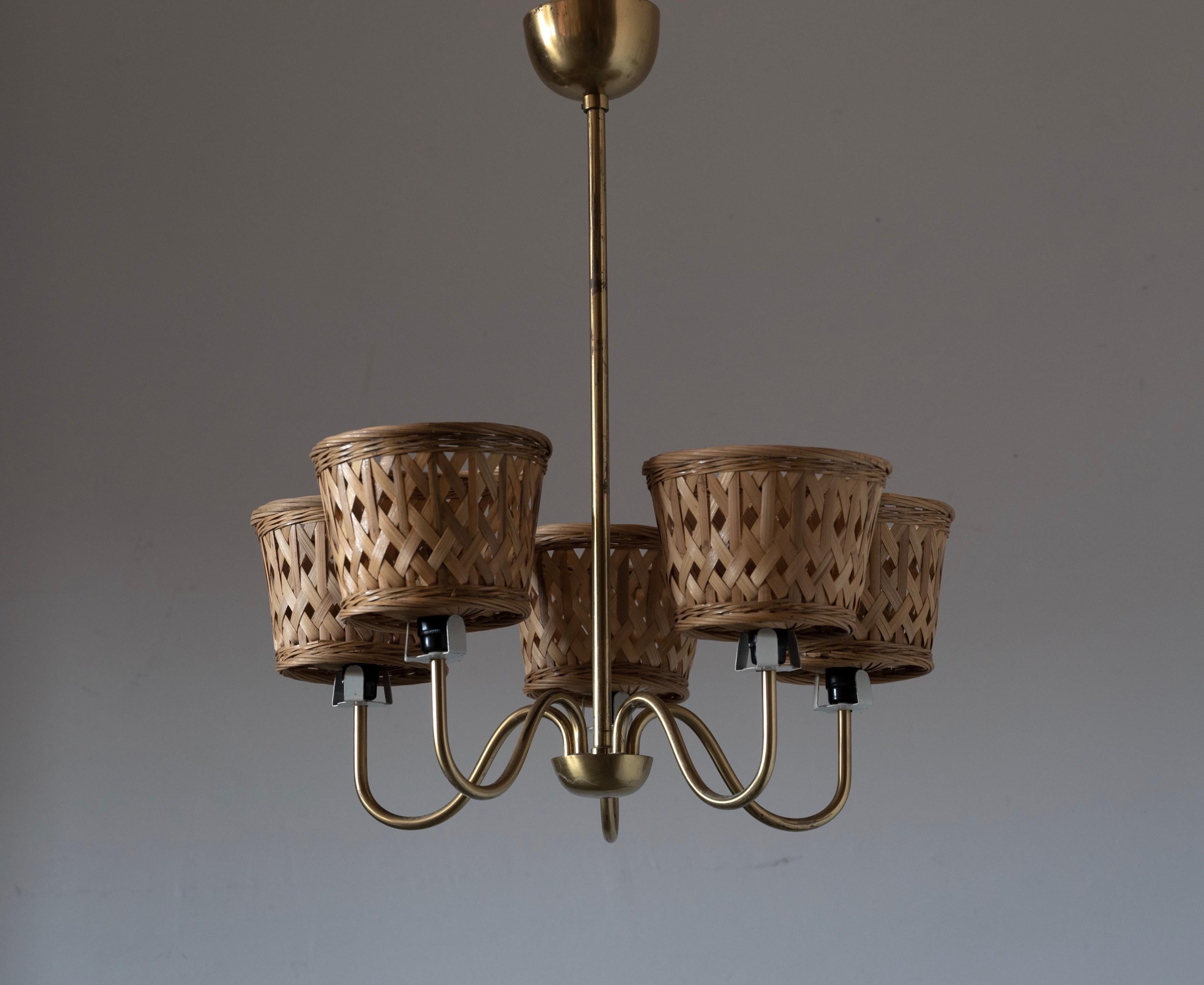 A small five armed chandelier, designed and produced in Sweden, 1950s. In brass with assorted vintage rattan lampshades. Mounted atop lacquered metal fittings likely originally mounting glass diffusers.

Measurements are from the bottom of the