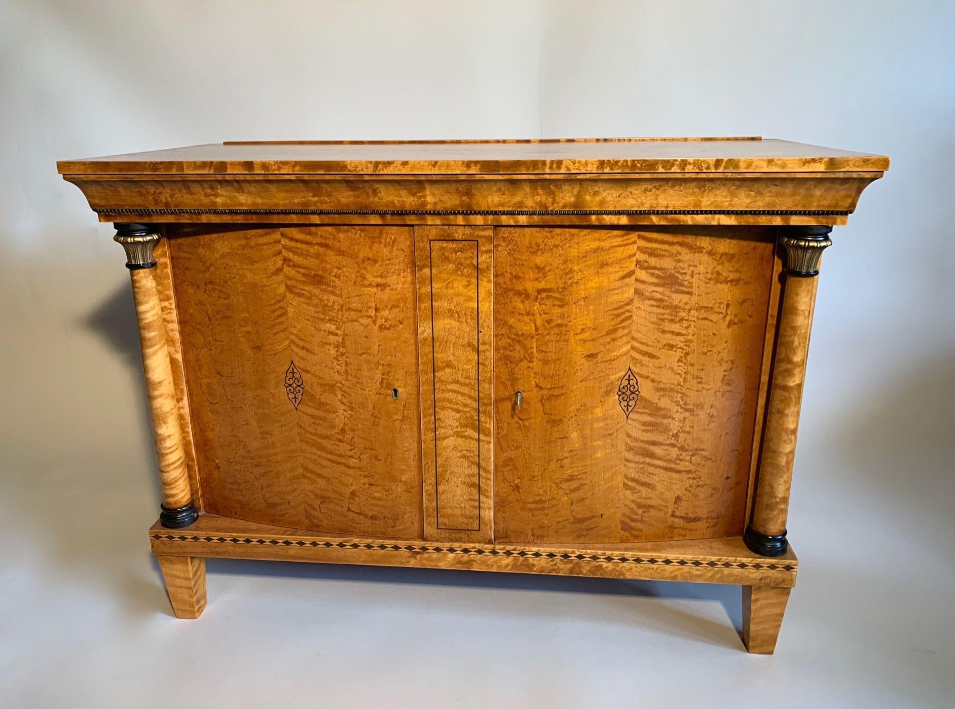 Swedish flame birch Biedermeier sideboard. The doors are curved and are flanked by full turned columns which have hand carved gilded corinthium capitals. the doors and base have an ebony inlaid decoration. The top under edge has a nulling hand