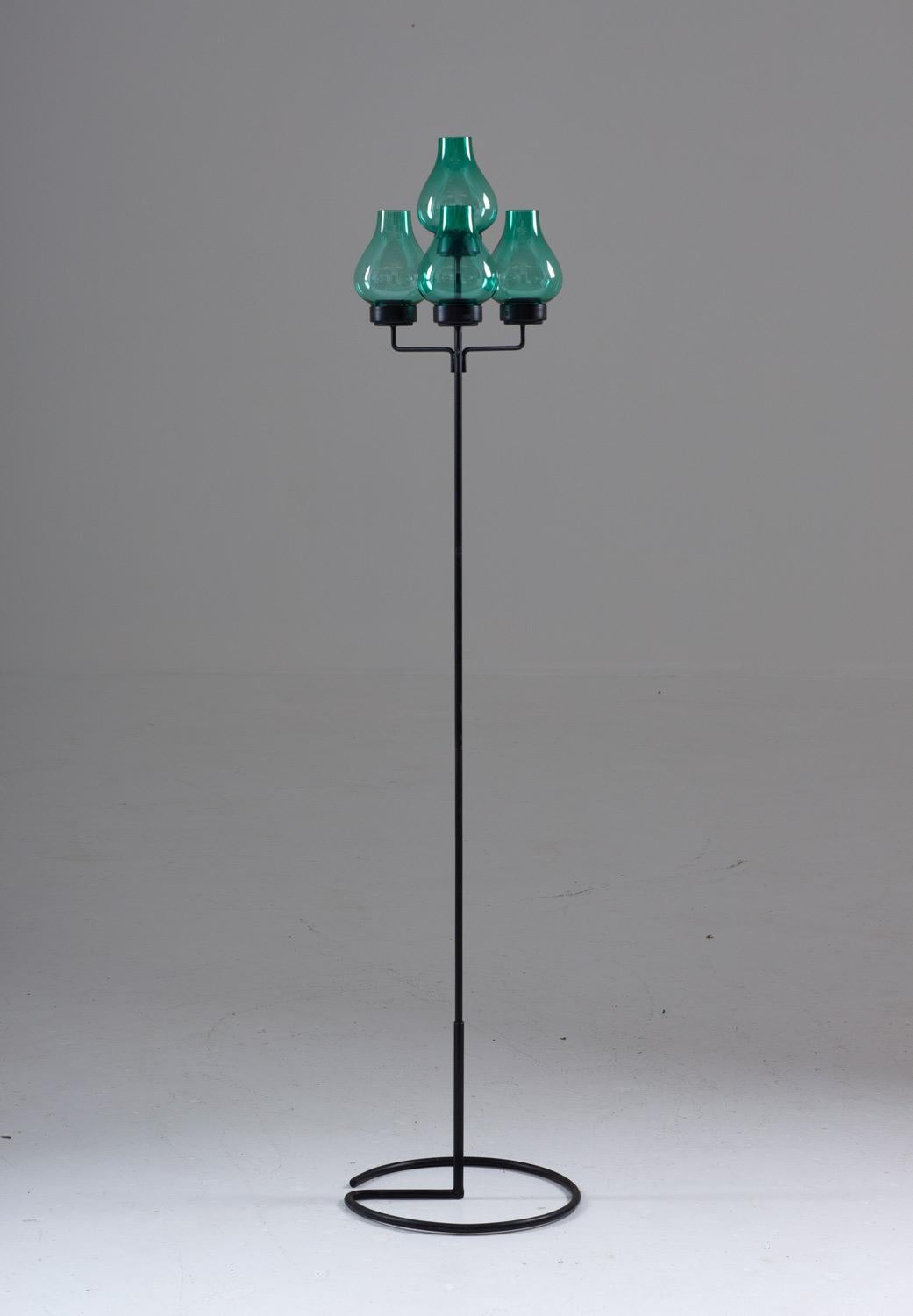 Rare floor standing candelabra in iron and glass by Gunnar Ander for Ystad Metall.
This candelabra consists of three connected iron sticks, supporting four green glass shades. The lower stick is made to be able to put in the ground for outdoor use.
