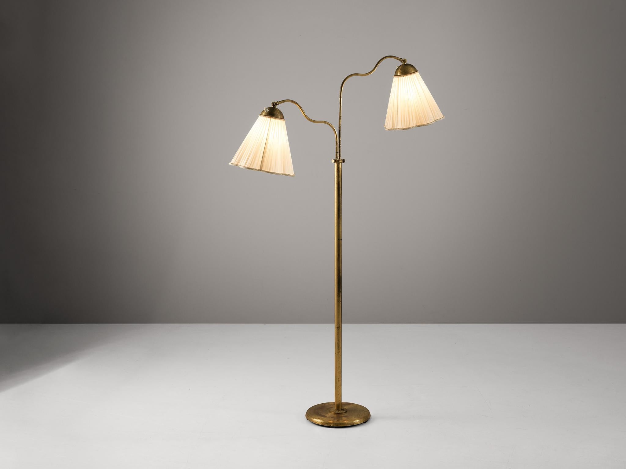 Floor lamp, brass, fabric, Sweden, 1940s.

This graceful Swedish floor lamp contains two arms, each with a flower-like thin white fabric shade that creates a soft warm light partition. The base and stem are made of brass that shows a beautiful