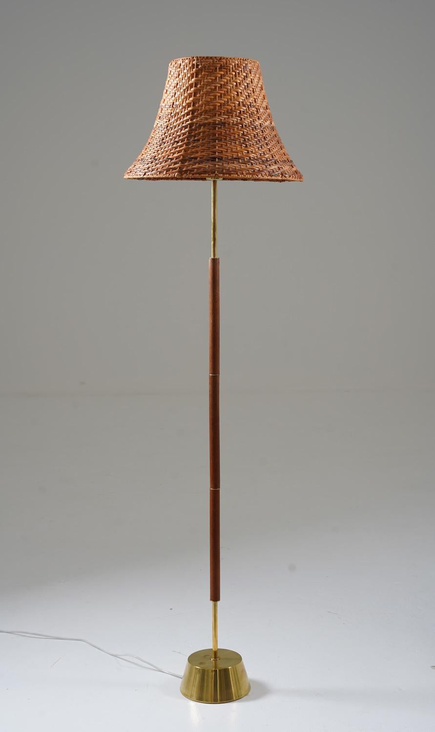 Simple and elegant floor lamp in teak and brass by Boréns, Sweden. 
The lamp features a heavy brass base, supporting a rod in teak with brass details. The lamp comes with a vintage rattan shade. 

Condition: Very good original condition, a few