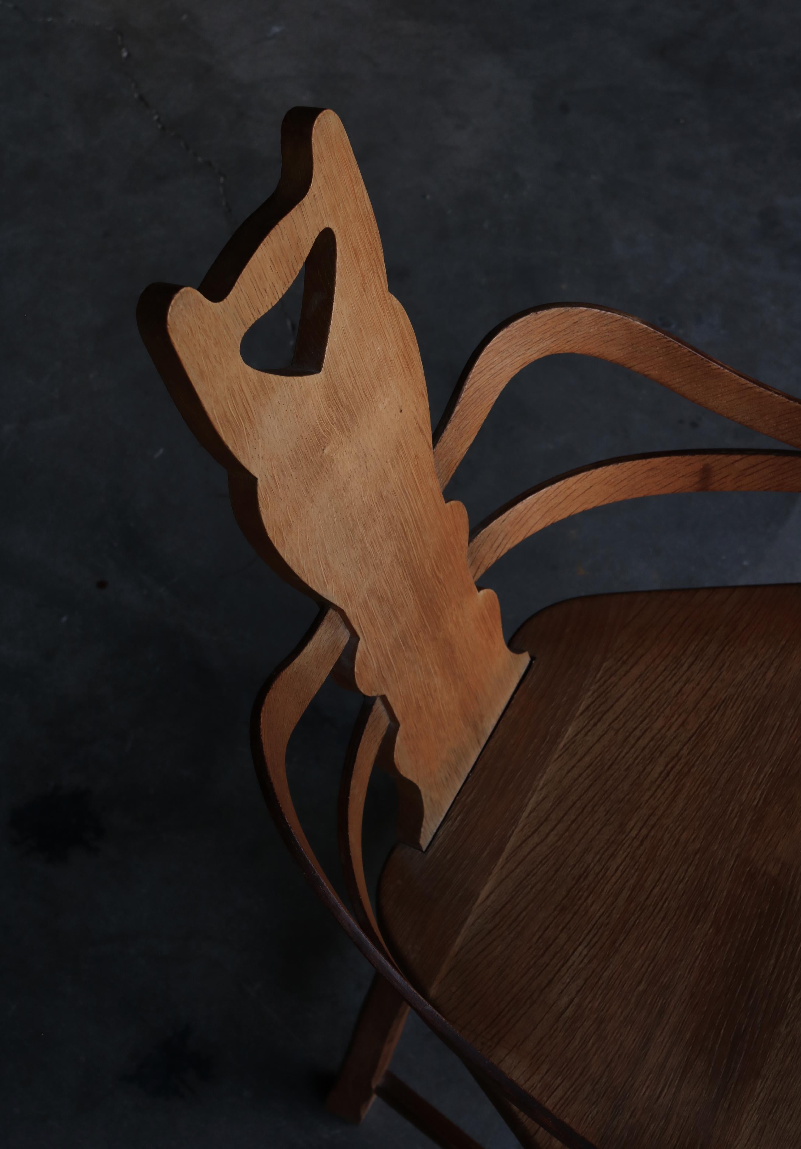 Charmante et inhabituelle chaise d'art populaire suédois fabriquée par un artisan qualifié au début du 20e siècle. La chaise est construite en chêne massif et les accoudoirs décoratifs sont en stratifié de chêne. Le dossier présente une forme