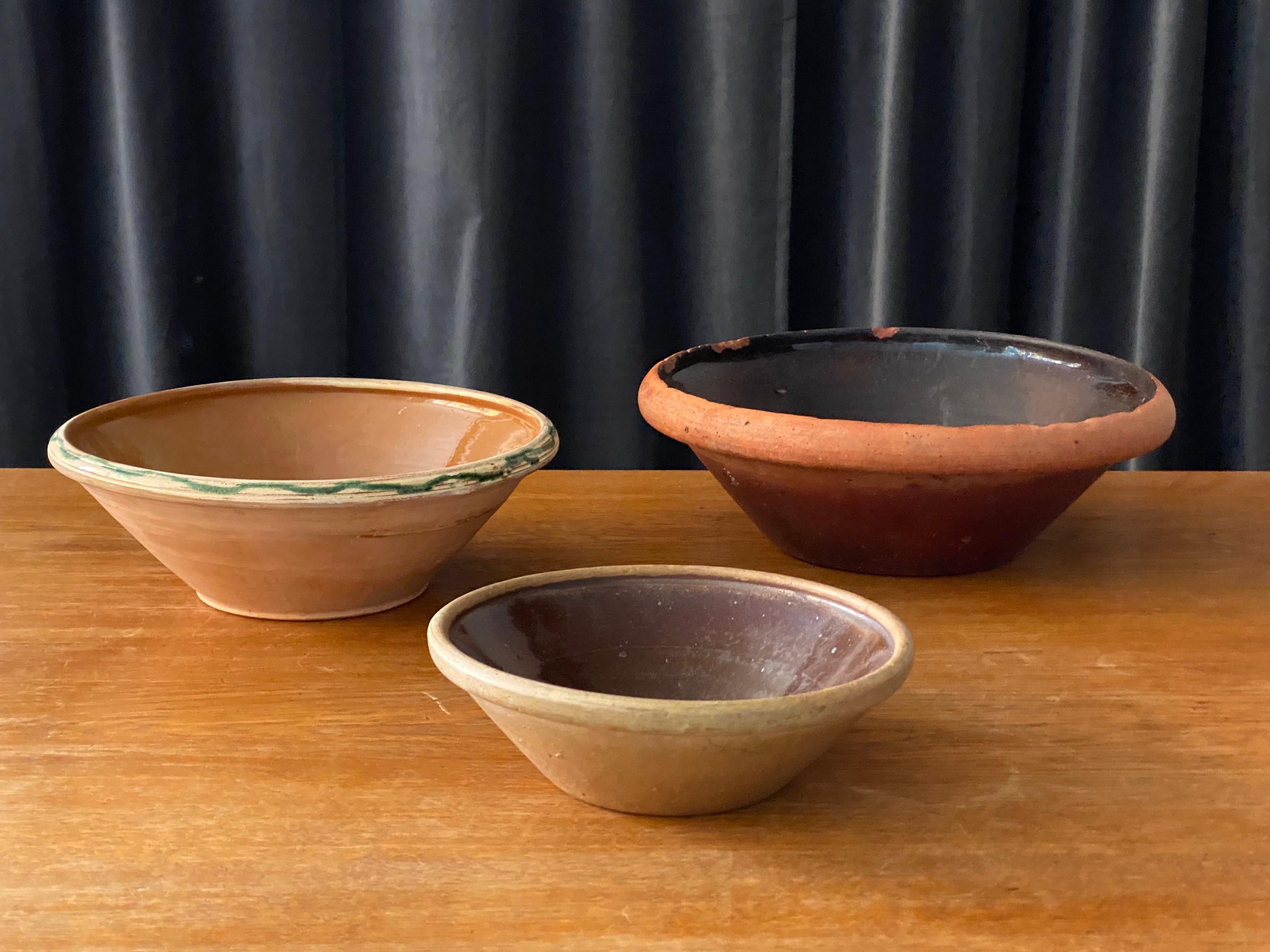 An antique and unique set of farmer’s ceramic pottery bowls. Produced in Sweden, 19th century. Examples from one collection, in different glazes with hand painted details. 
 
Dimensions large to small (in cm):

D 32, H 11.5
D 17.75, H 10.5
D