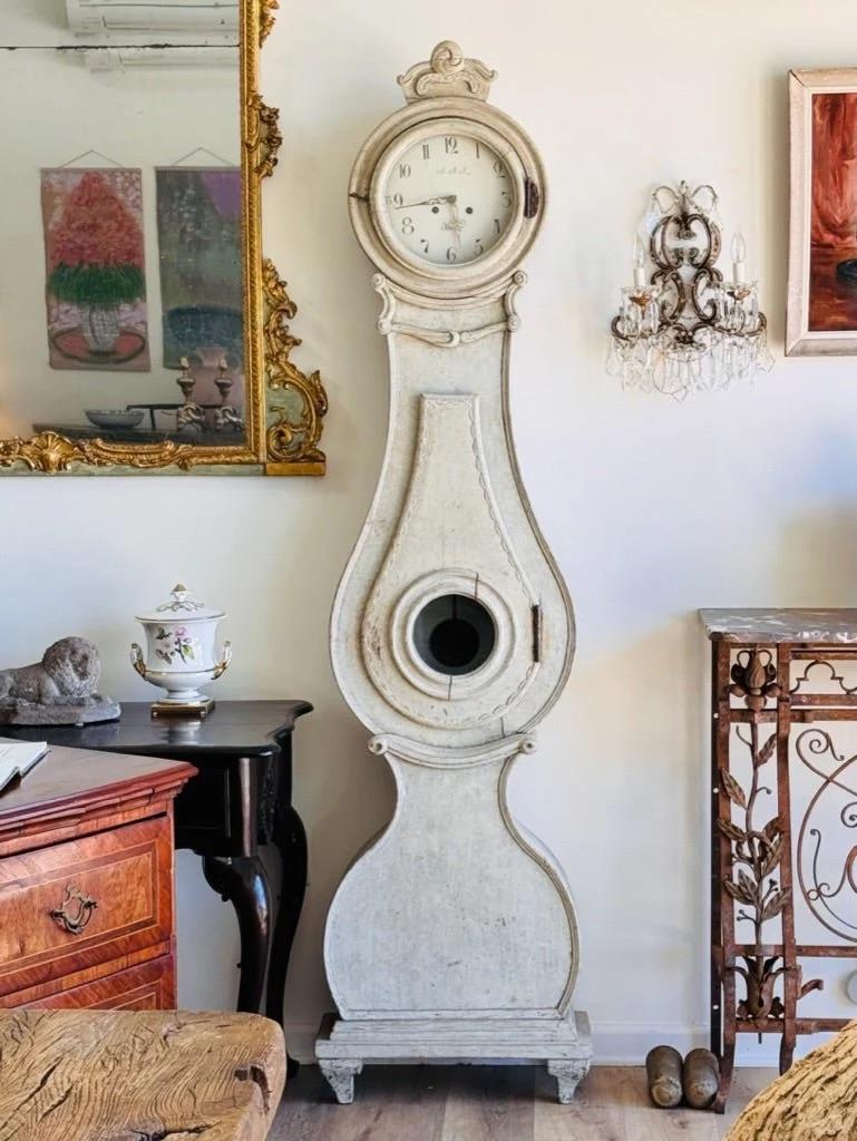 Elegant Swedish Fryksdahl grandfather clock with a raised base, c. 1820, Mora Clock off-white/cream painted.  Having enamel face and original movement.  This particular style of clock was only made in Fryksdalen, Värmland, located in west Sweden on