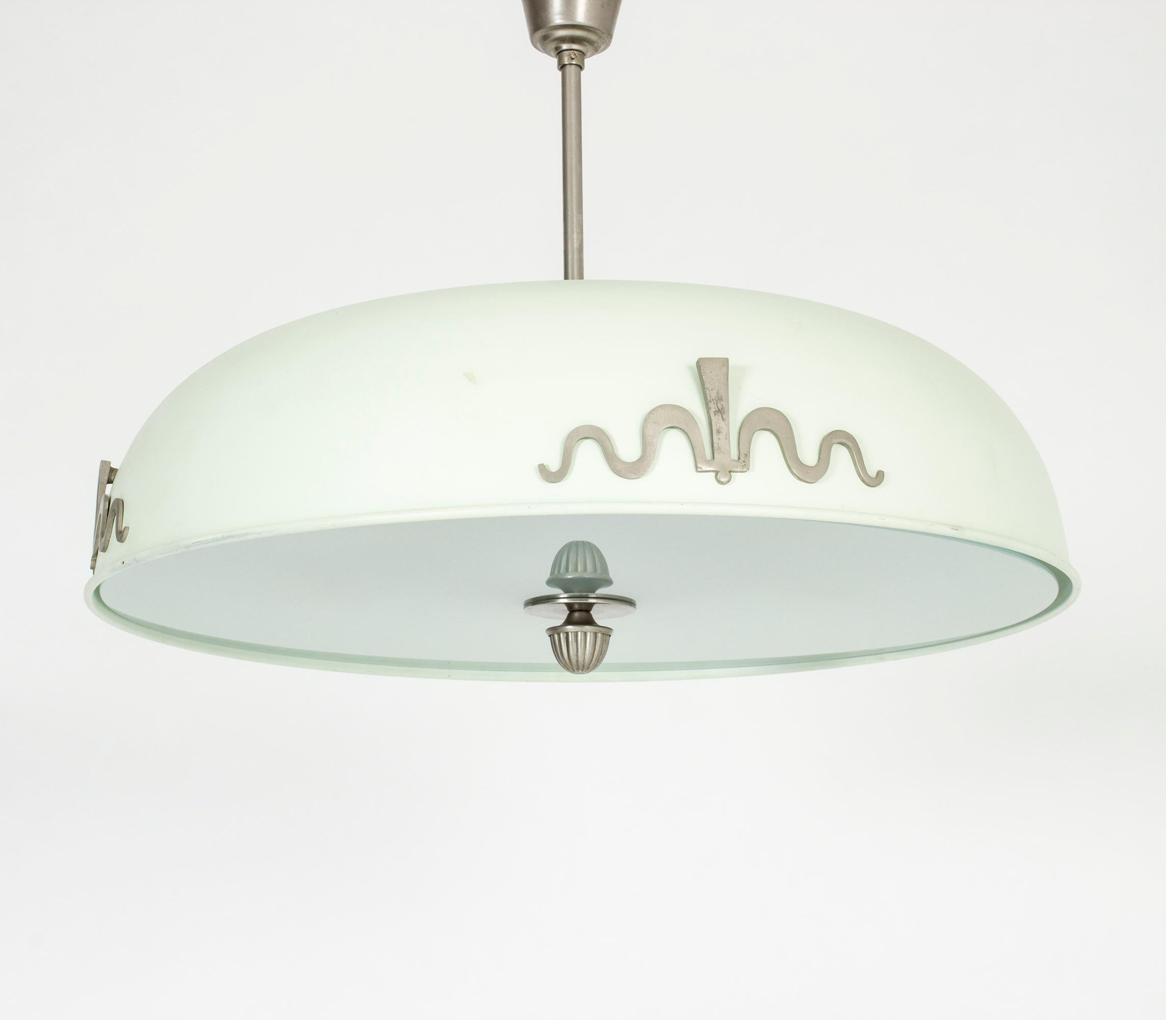 Beautiful metal and glass ceiling lamp, made in Sweden in the 1930s. Lacquered pale green with metal appliqués and a glass disk shielding the downward light. Three-light sources on the top create an uplight.