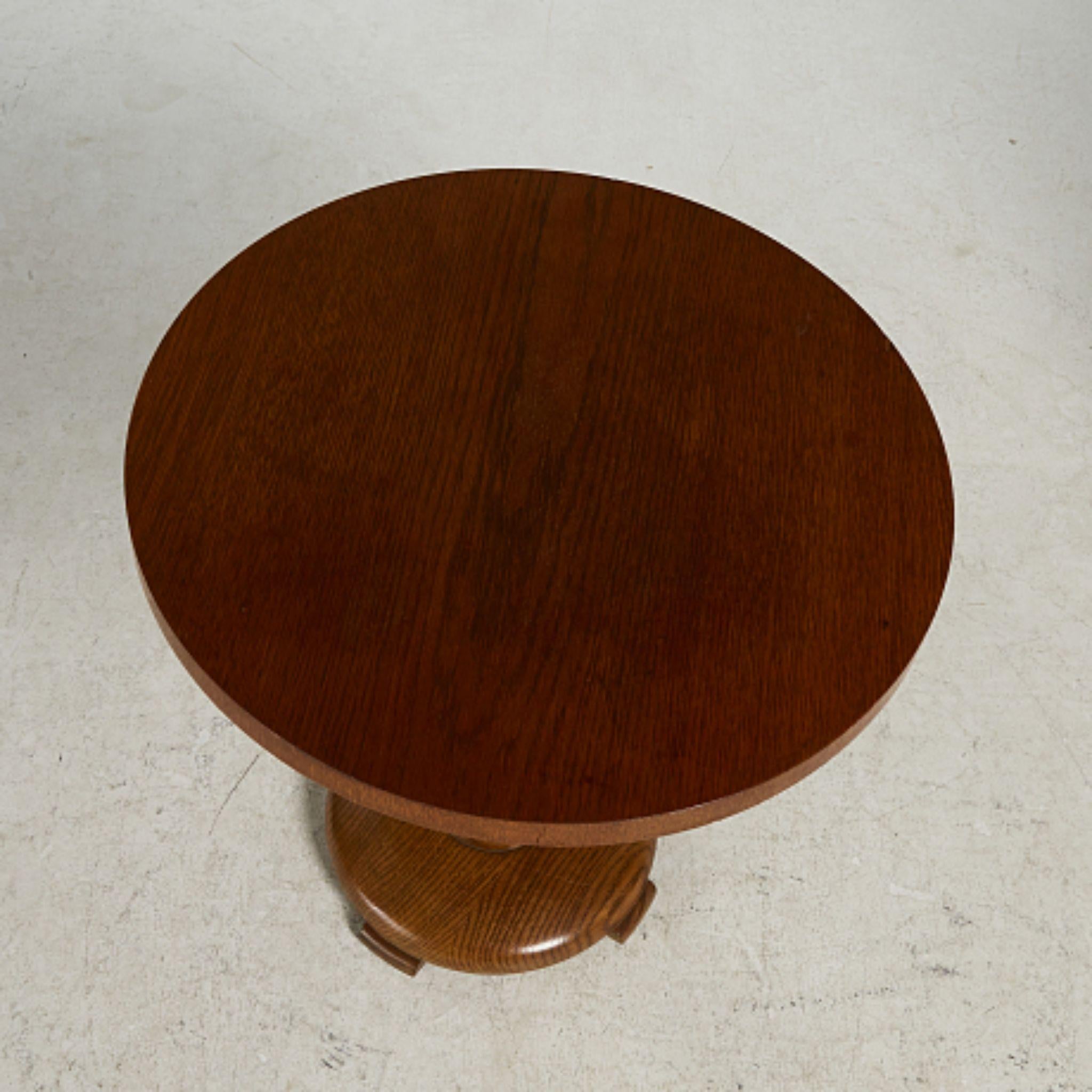This Swedish Functionalist pedestal table from the 1940s features a round oak top supported by a central turned column that rises from a sculptural disc base set on four small block feet. The design reflects the clean, modern lines of the Swedish