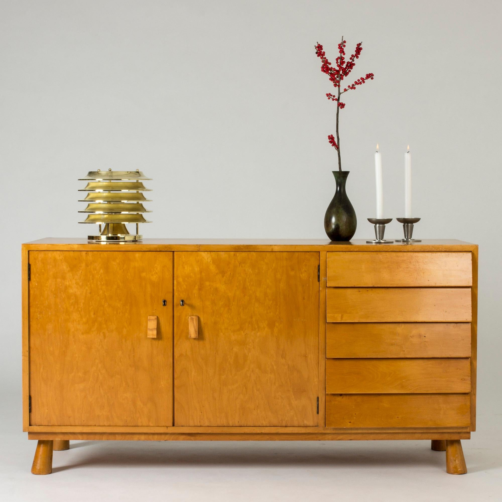 Striking Swedish functionalist sideboard from the 1930s. Neat size, with a set of drawers with slanted fronts on one side. Matching slanted handles on the cabinet doors. Chunky, angled legs both harmonize with the sideboard’s overall lines and