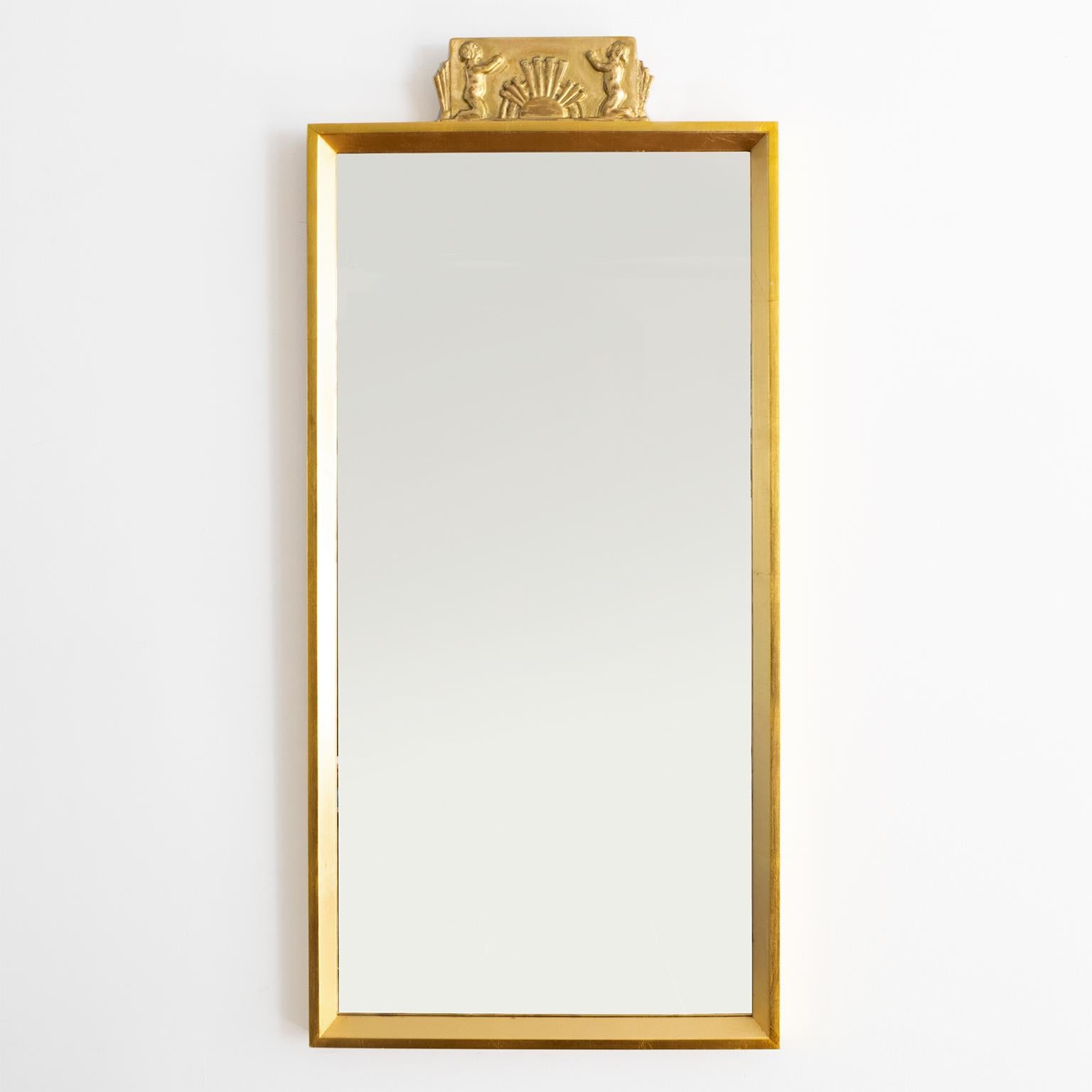 Scandinavian Modern wall mirror with carved giltwood element showing children flanking a rising sun. 

Measures: Height 39”, width 18”, depth 1.5”.