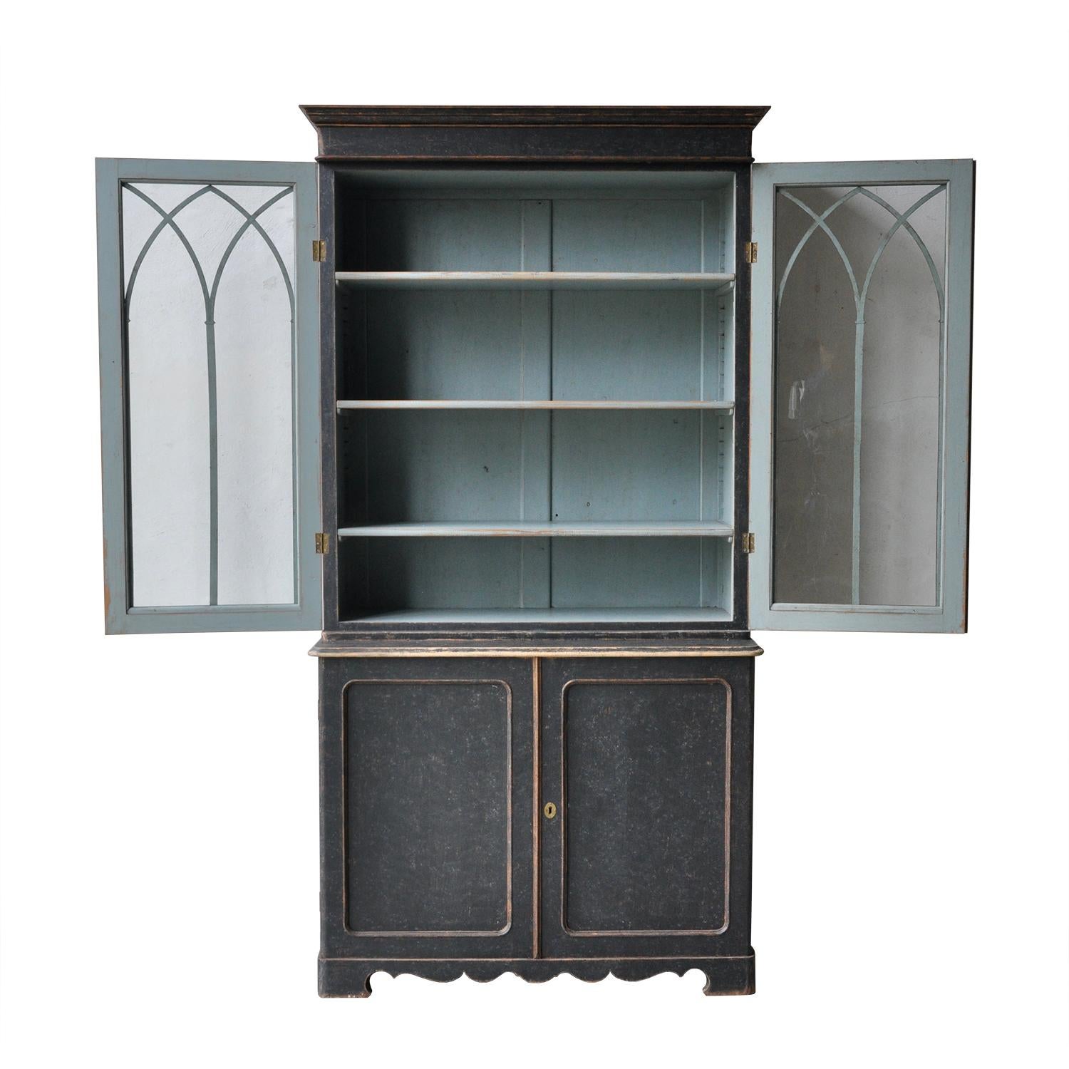 Swedish 19th century bookcase with two glazed doors and gothic detailing, opening to four bookshelves. Below, two further doors open to more storage. This piece has been repainted in black, with a blue interior. The shelves are adjustable in both