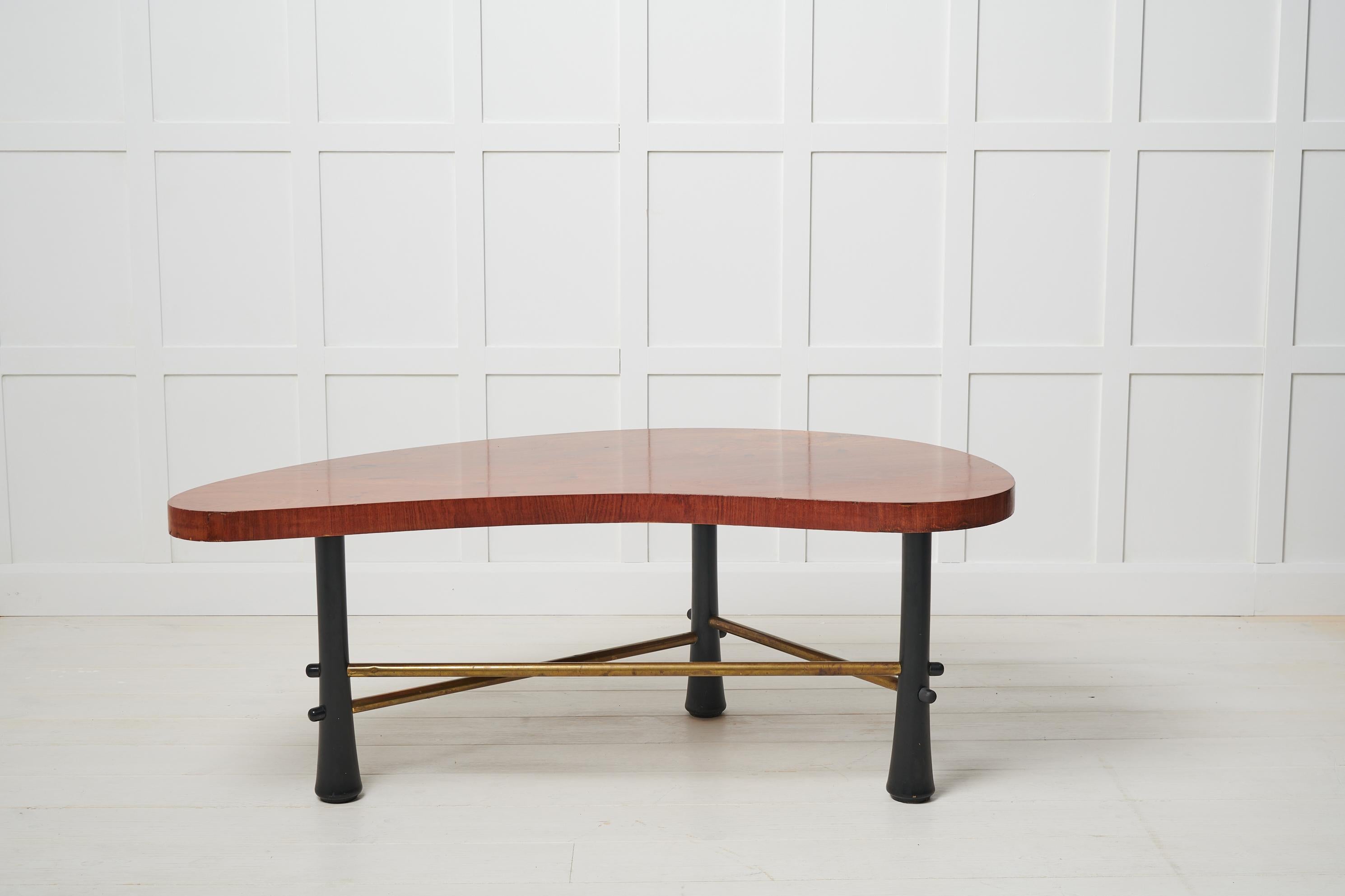 Table basse Grace suédoise des années 1930-1940. La table a un plateau en forme de rein plaqué en noyer et des pieds noirs avec un croisillon en laiton. La table présente une élégante forme incurvée qui s'accorde avec le noyer organique du plateau.