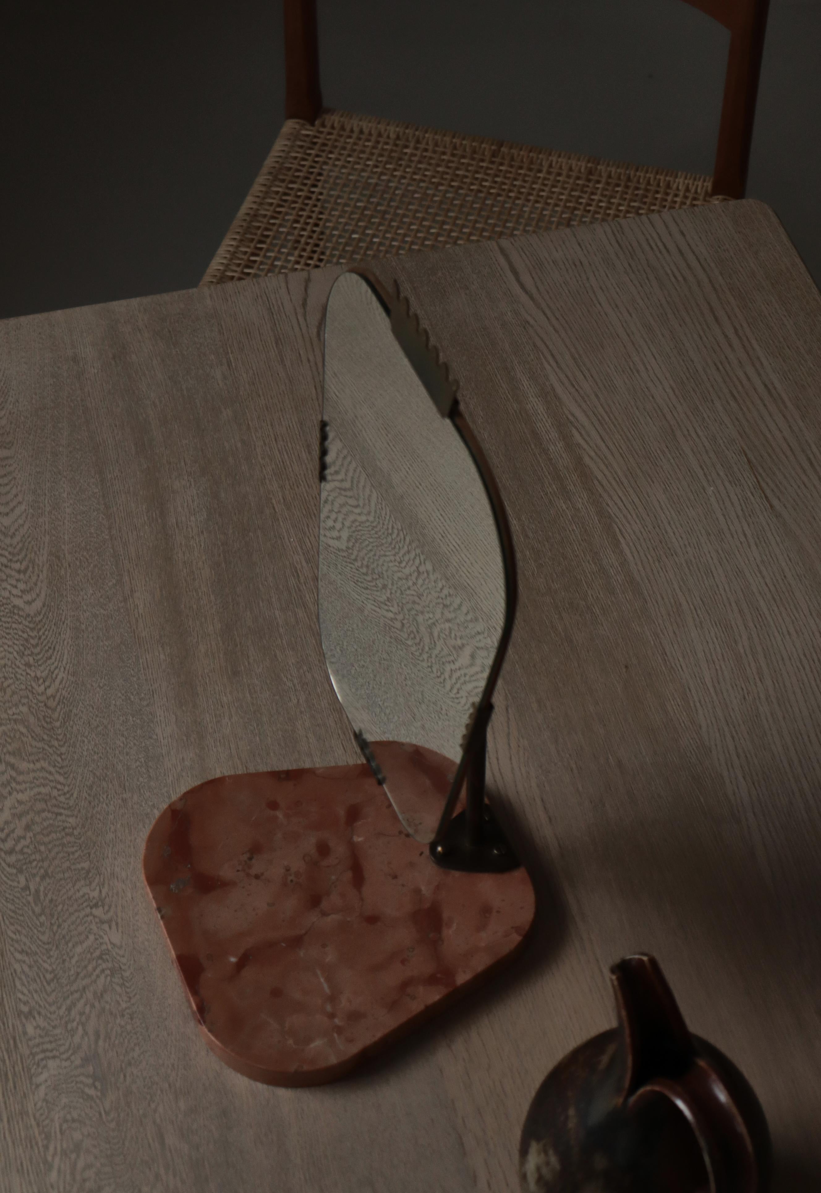 Un élégant miroir de table Grace suédois des années 1940, qui se distingue par sa géométrie équilibrée et sa matérialité raffinée. Le miroir repose sur un socle en marbre sculpté dans des tons chauds de rose et d'ocre, dont les veines naturelles