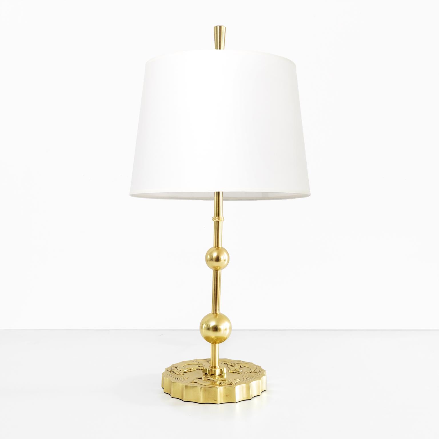 A Swedish Grace, Art Deco table lamp in polished brass. The rounded base has a relief of mermaids ridding dolphins in the a sea. Two brass spheres rise above on a brass stem which meet a double socket cluster. Newly restored, rewired for use in the