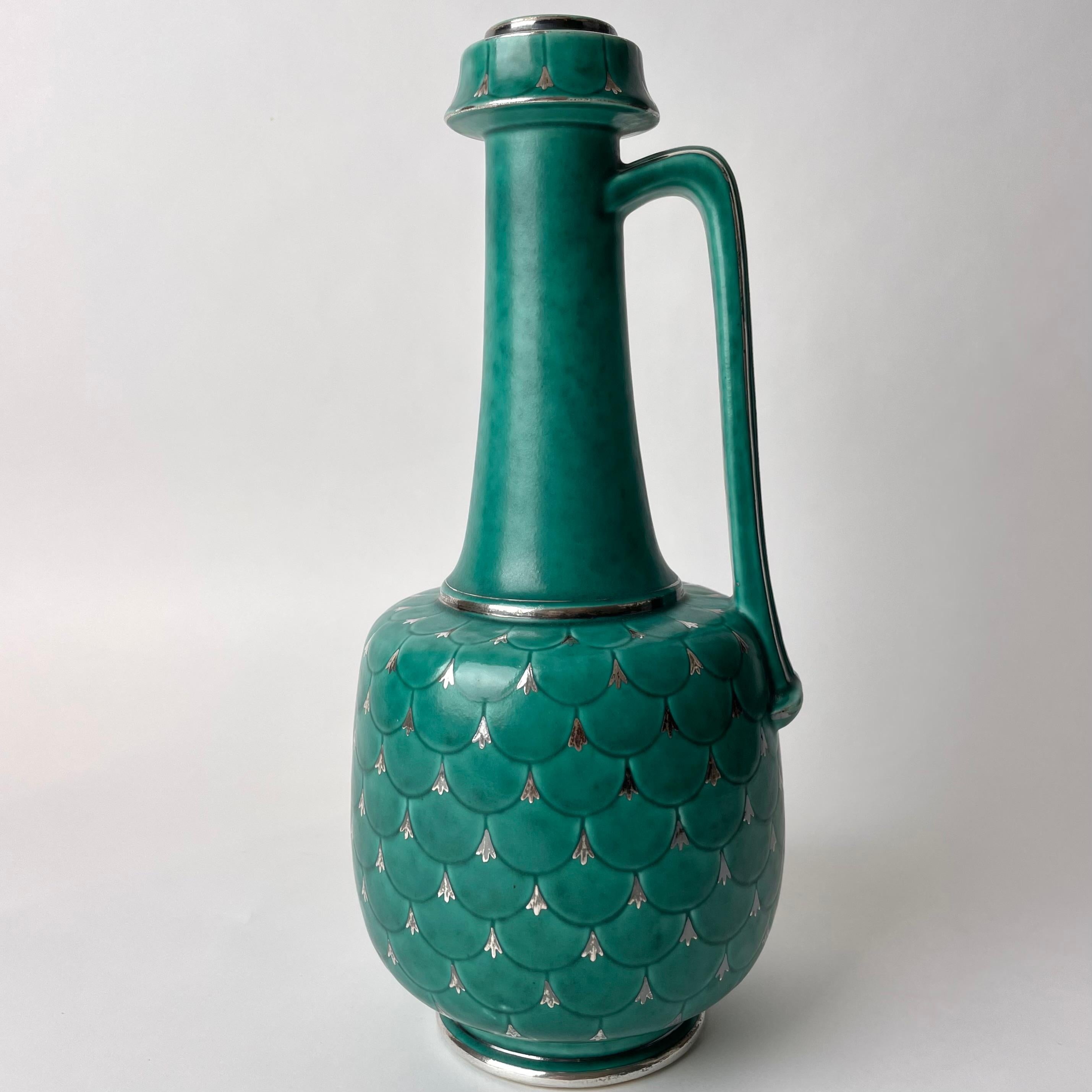 Swedish Grace Ceramic Handle Vase, Argenta collection from the prominent Swedish Gustavsberg company, 1930s-1940s Sweden

This beautiful Swedish Grace vase in turquoise ceramics with silver details was manufactured by prominent Swedish Gustavsberg