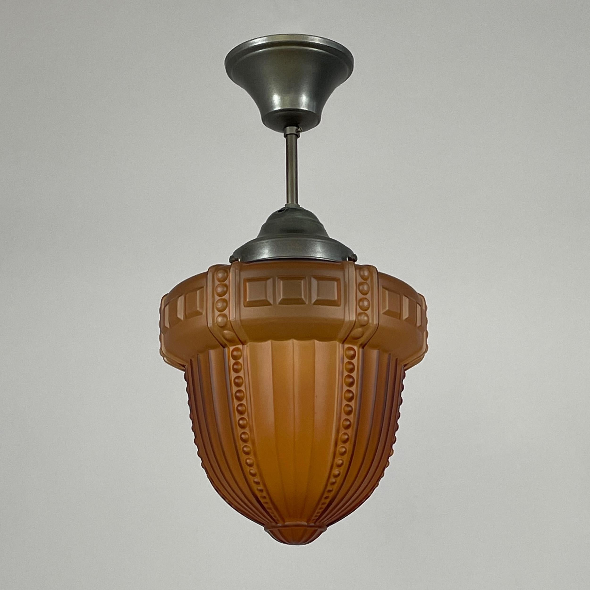 This Swedish Grace pendant was designed and manufactured in the 1920s to 1930s.

The light features a beautifully sculpted amber-colored glass shade with a striking Art Deco design, originating from Sweden in the 1920s. Its bold geometric patterns,